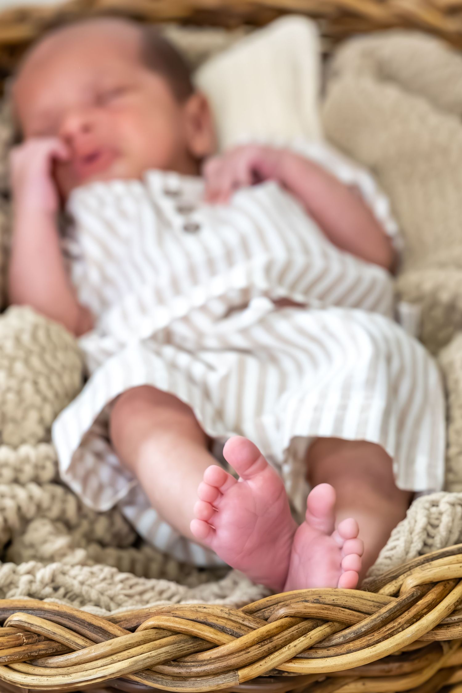 A newborn in white clothing rests peacefully on a woven basket surface.
