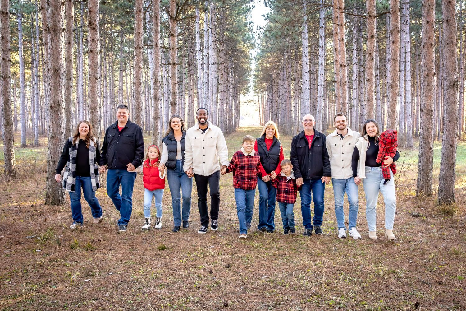 Extended family group photo taken in a pine forest with everyone wearing coordinated casual outfits.