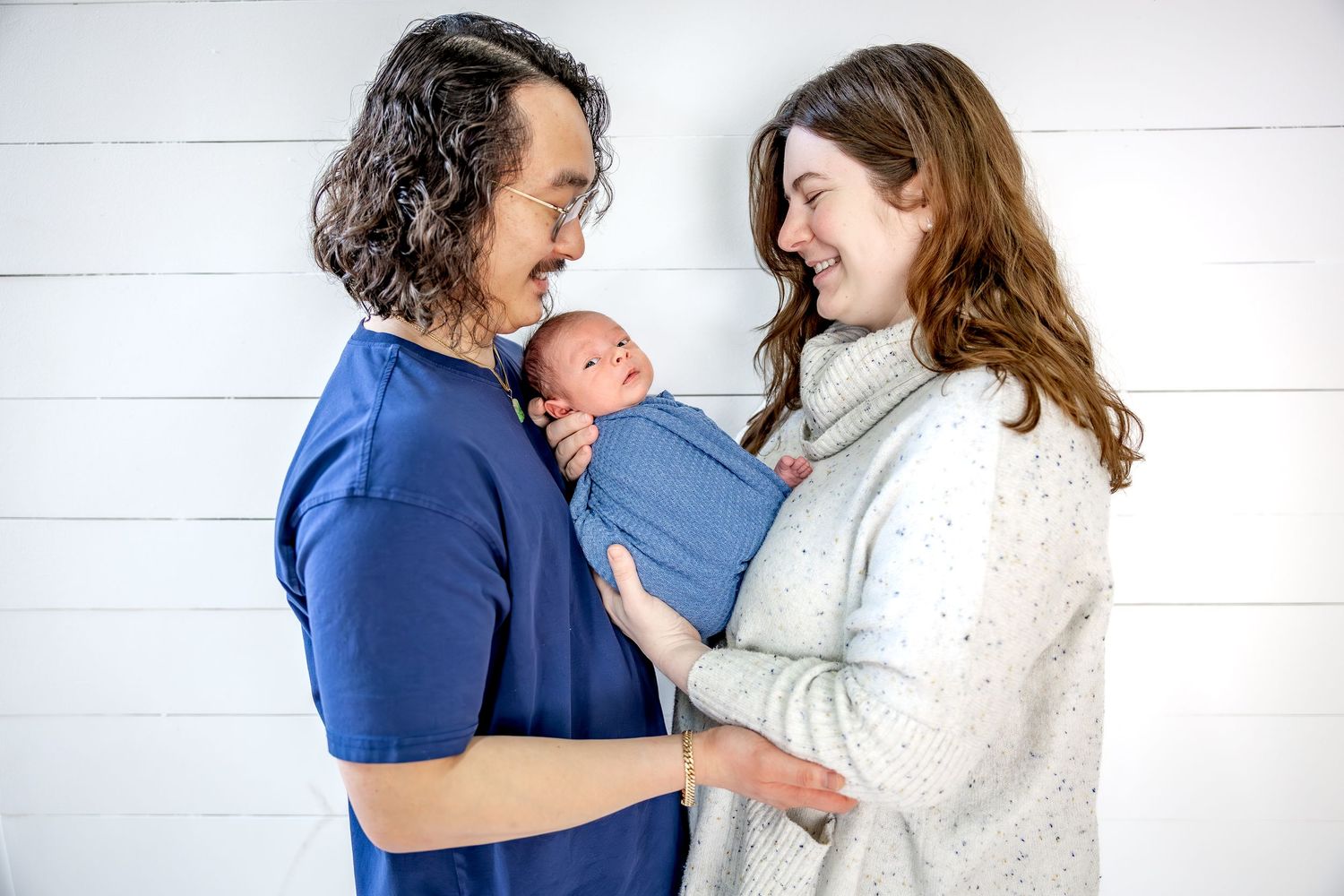 A couple shares an intimate moment while holding their newborn baby wrapped in blue.