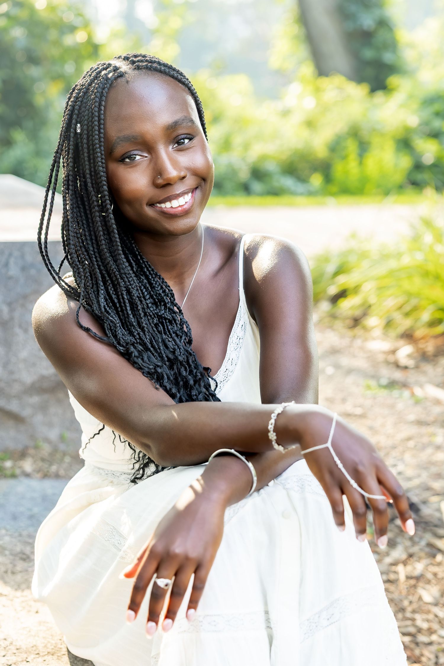 A person in a white dress smiles while posing in a natural outdoor setting.
