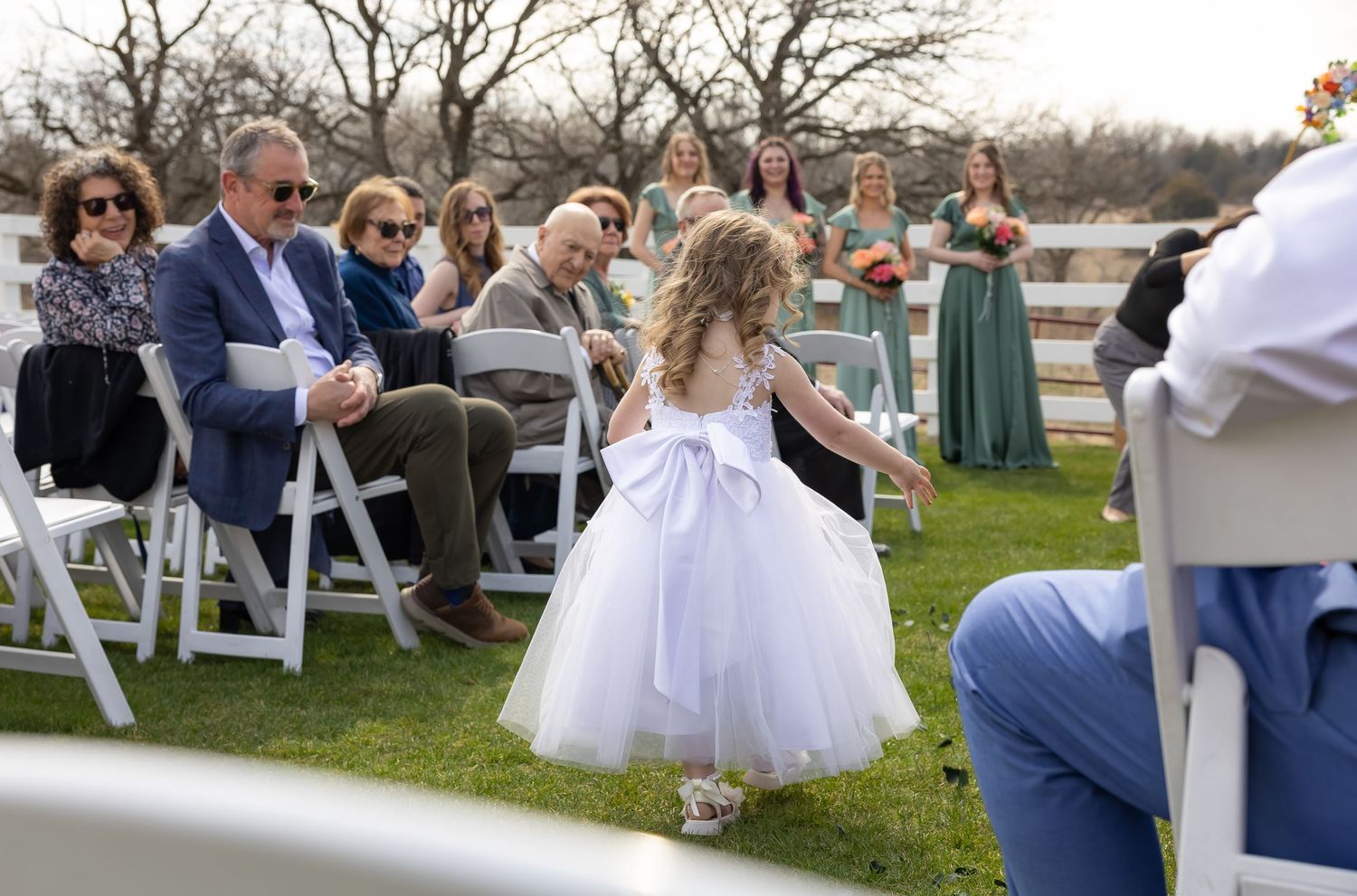 Outdoor wedding ceremony setup with white chairs and guests on a grassy lawn.