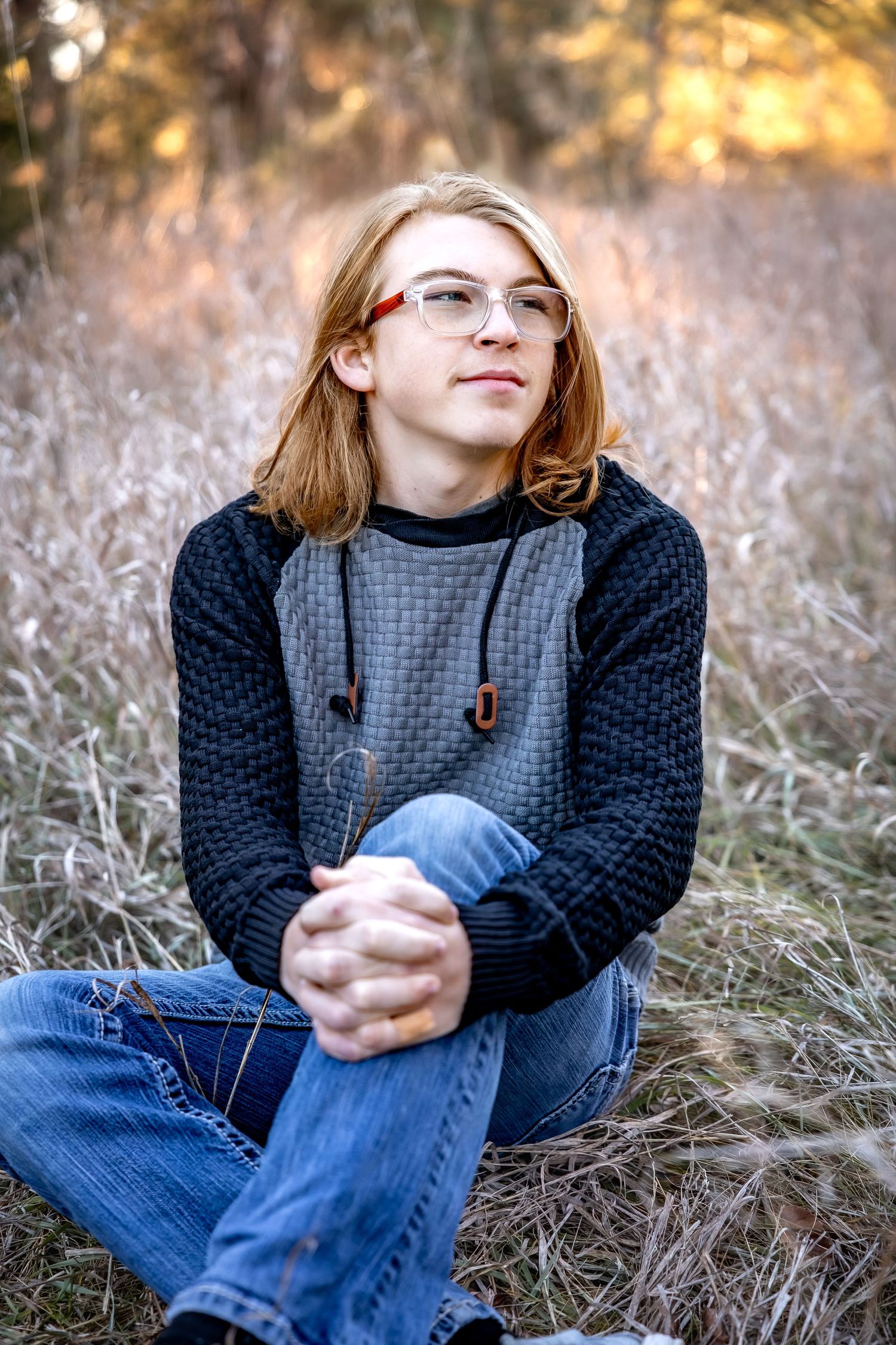 Person sits thoughtfully in autumn field during golden hour.