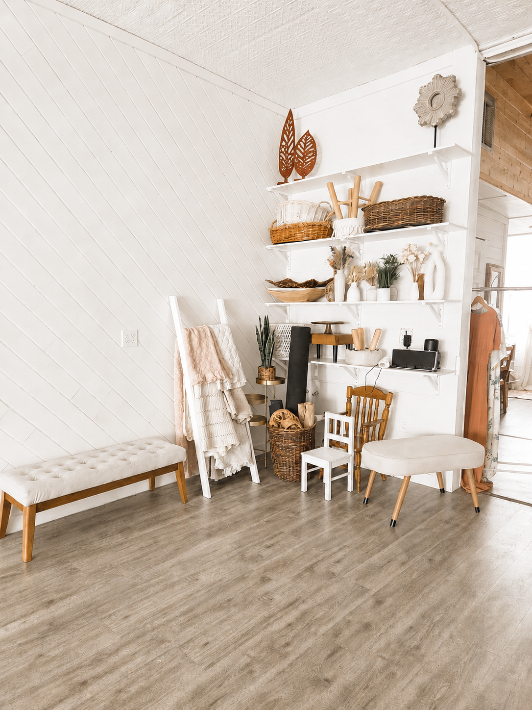 Bright boho farmhouse room with tufted bench, white shelves, wicker baskets, wooden decor, and light gray vinyl plank flooring.