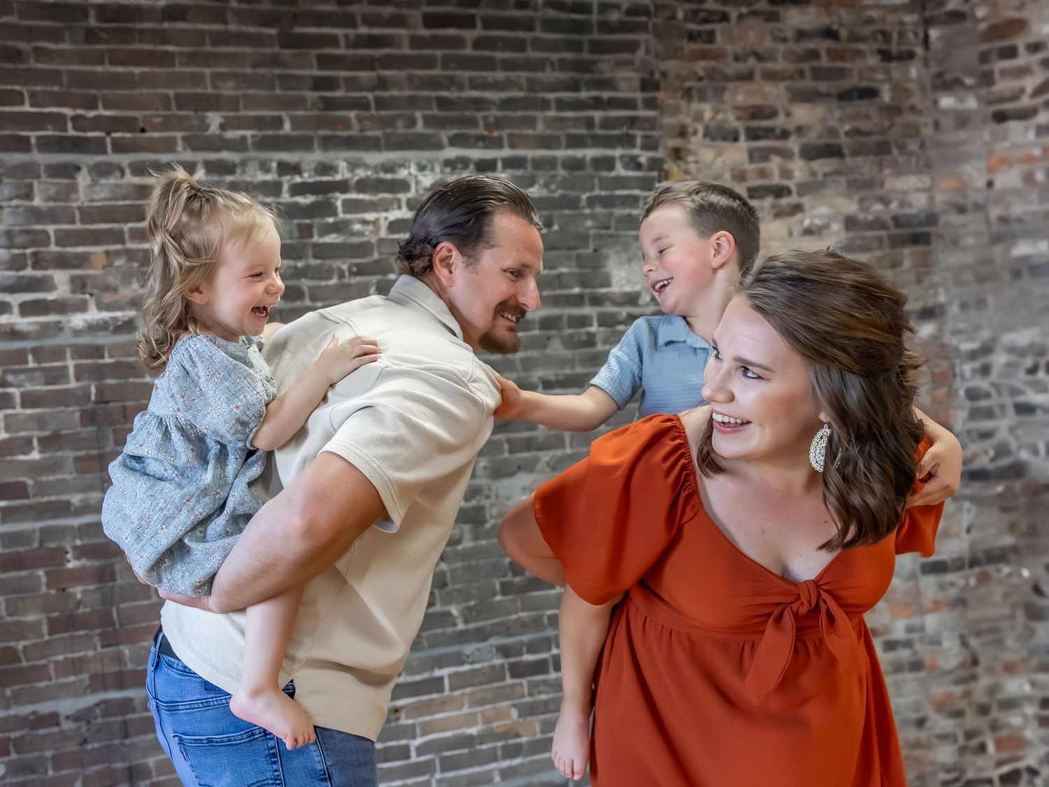 Playful family moments captured against rustic brick wall background.