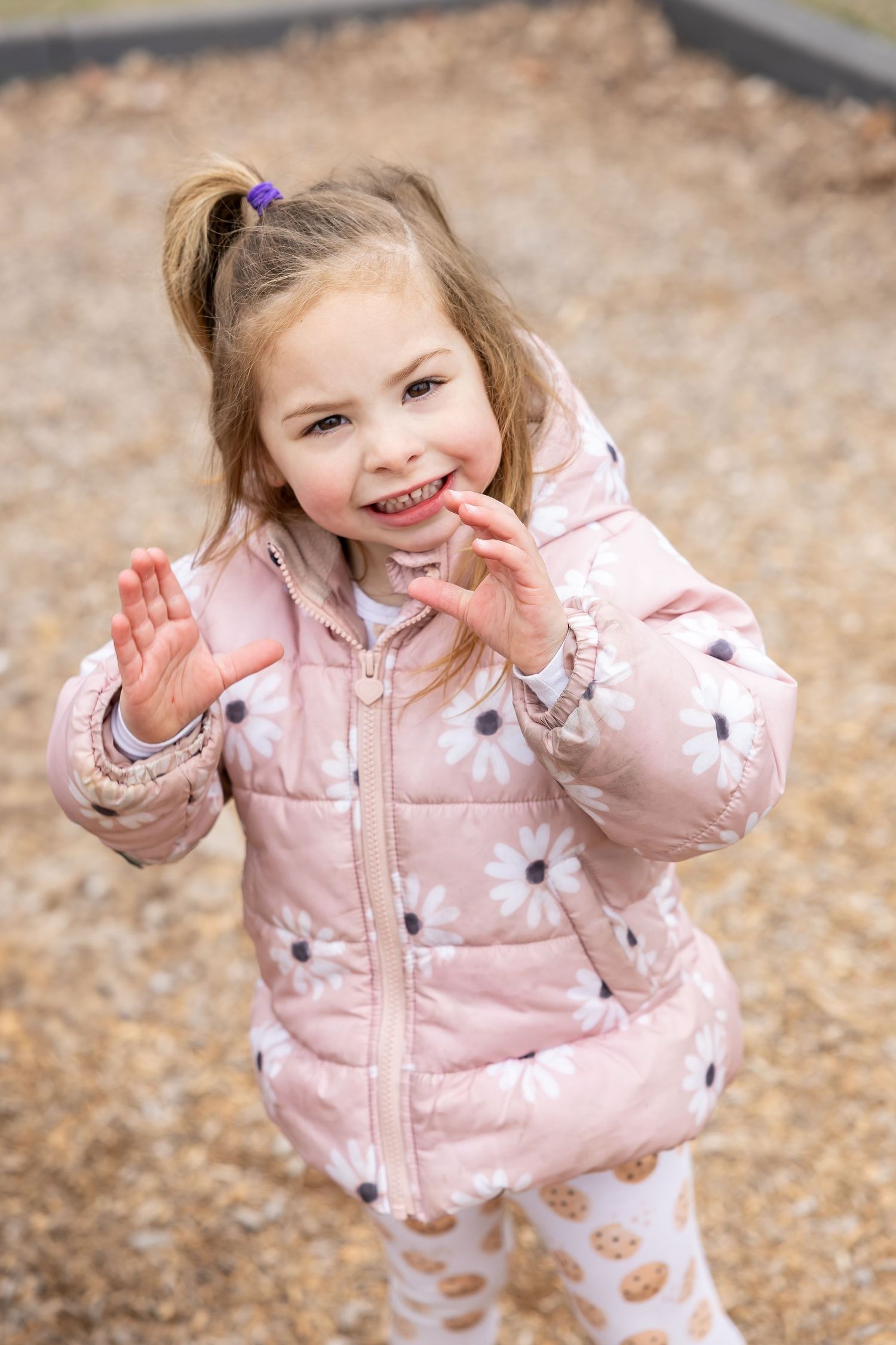 Young child wearing a pink floral puffer jacket plays joyfully outdoors in autumn.