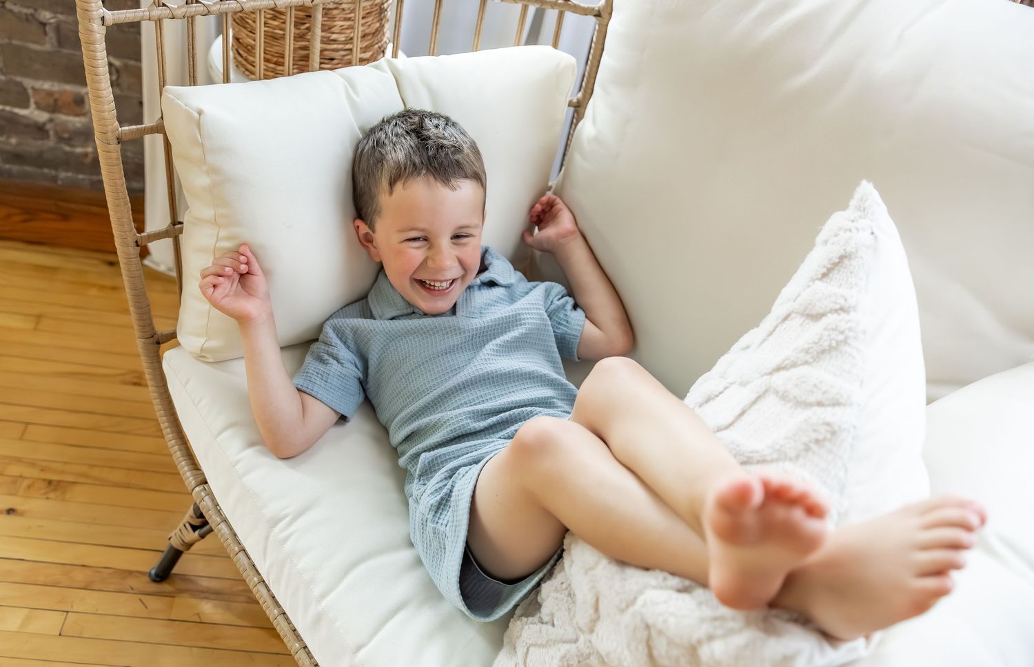 A child in a blue shirt lies on white cushions while laughing and showing their bare feet.