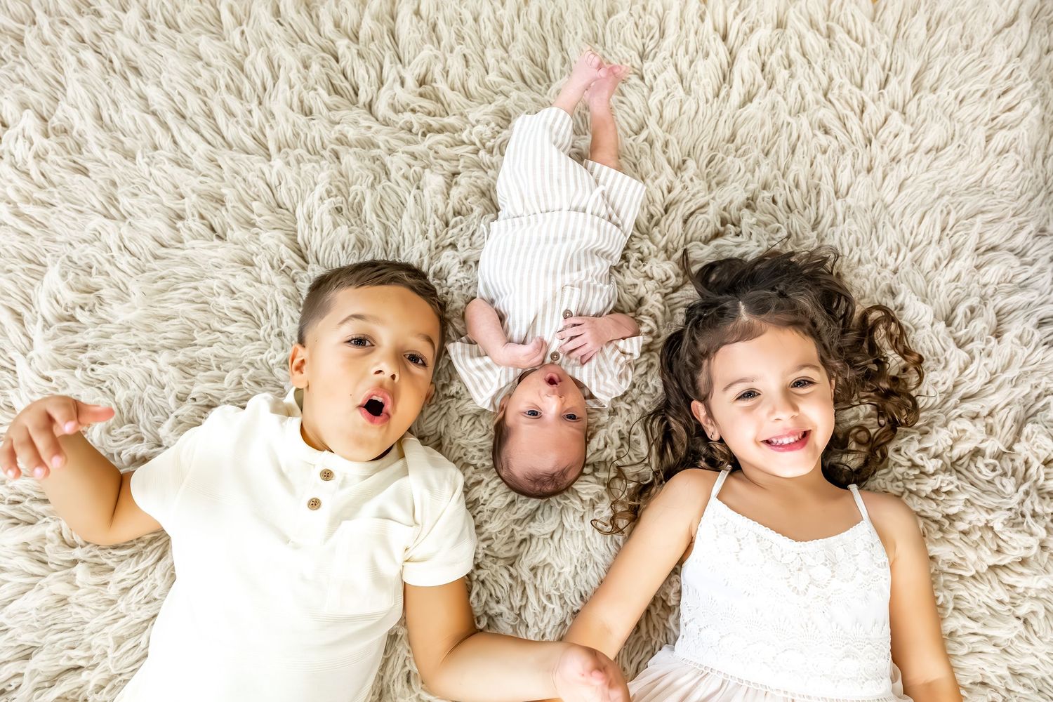 Lifestyle family photo showing siblings lying together on plush cream carpet.