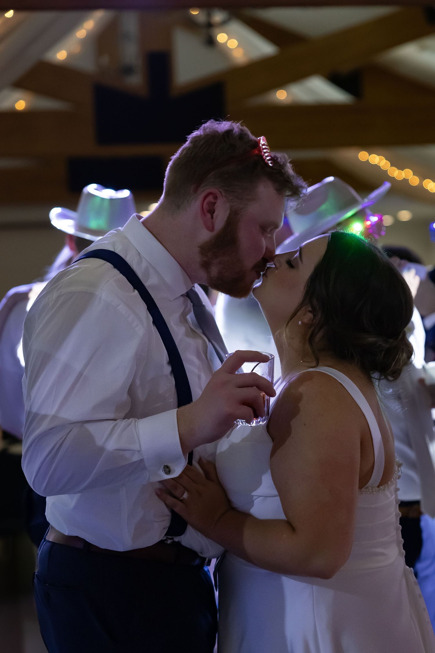 Couples dance together at a dimly lit wedding reception with colorful lights in the background.