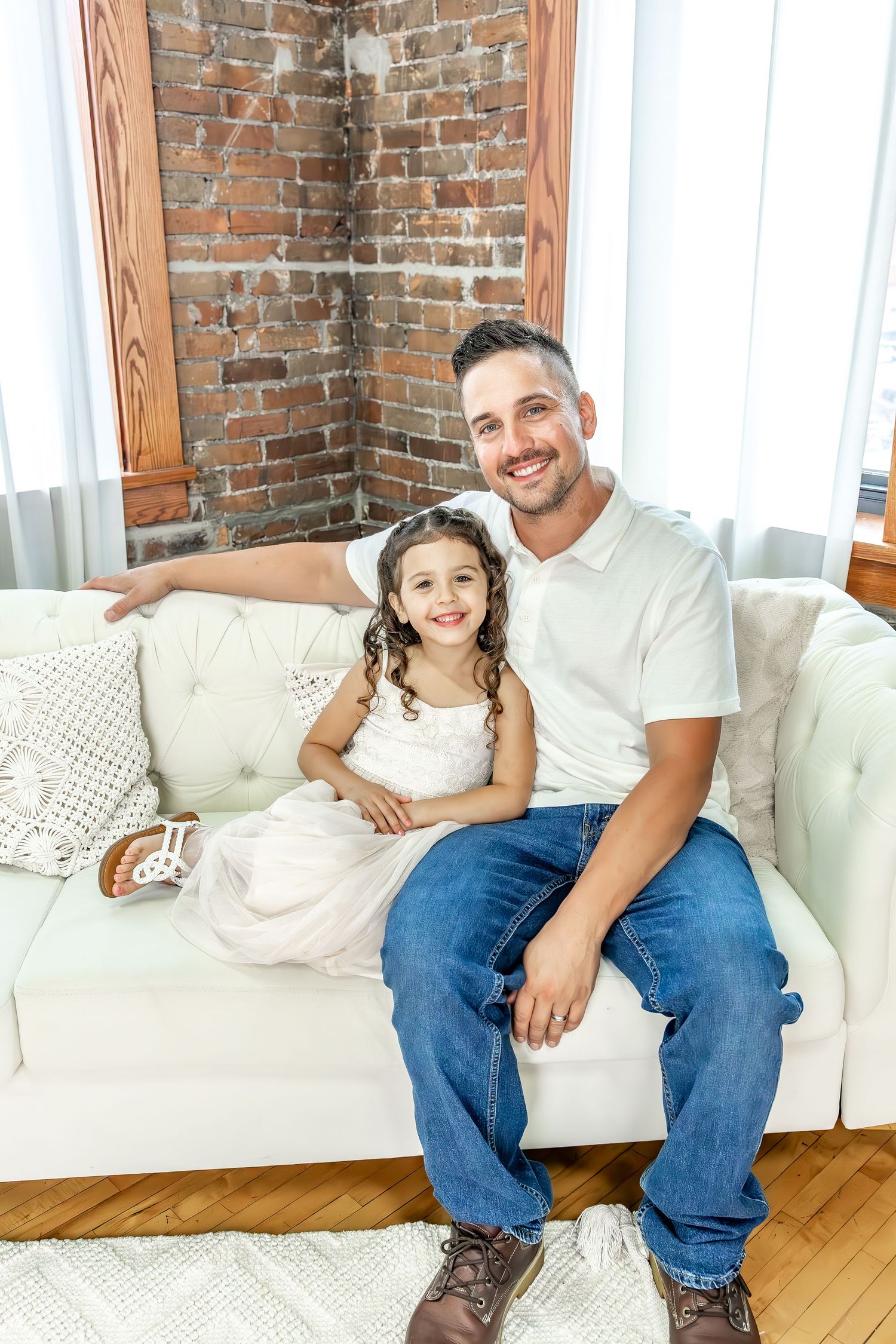 A family sits together on a white tufted couch against exposed brick walls.