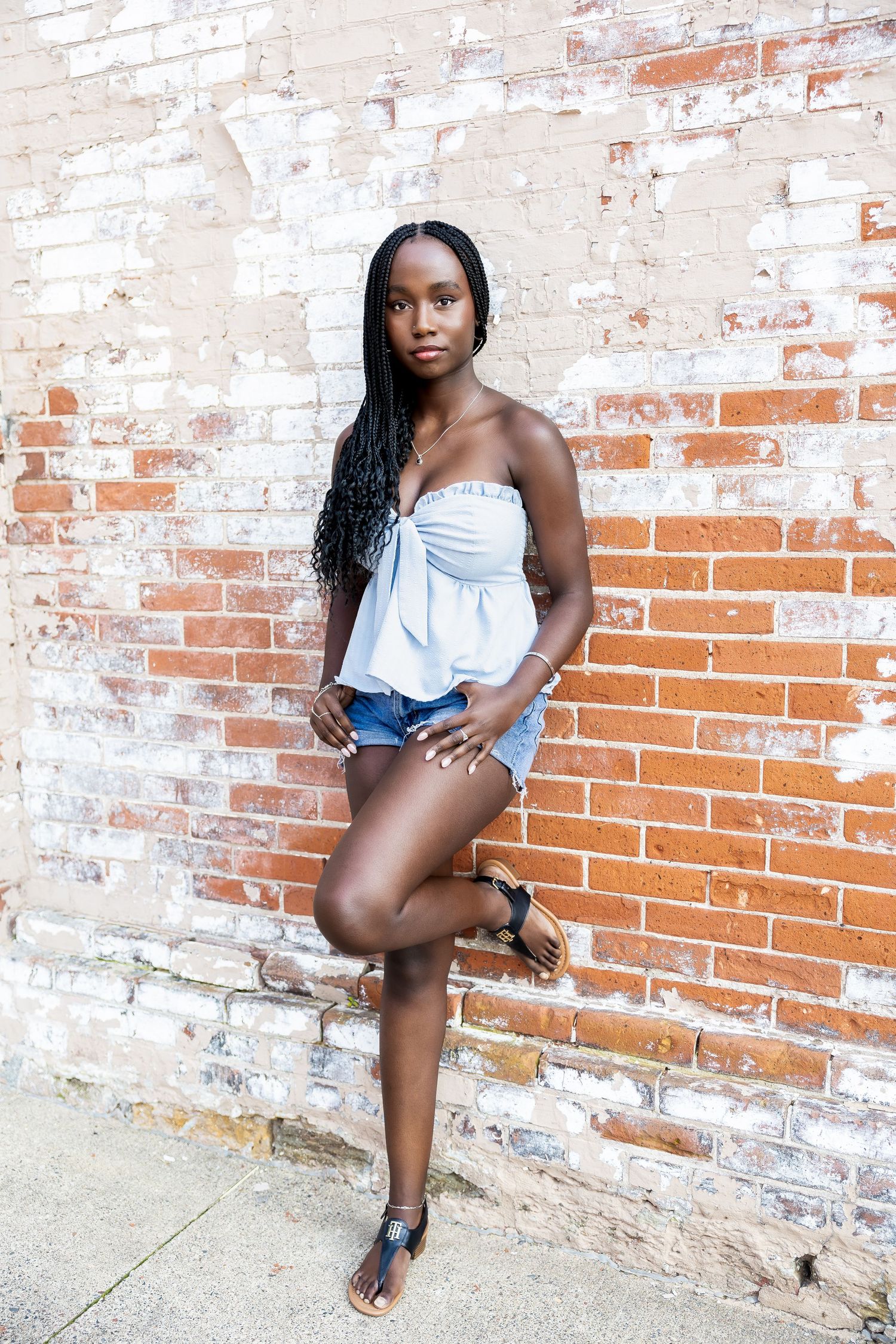 A person in a blue top poses against a weathered brick wall during a photo session.