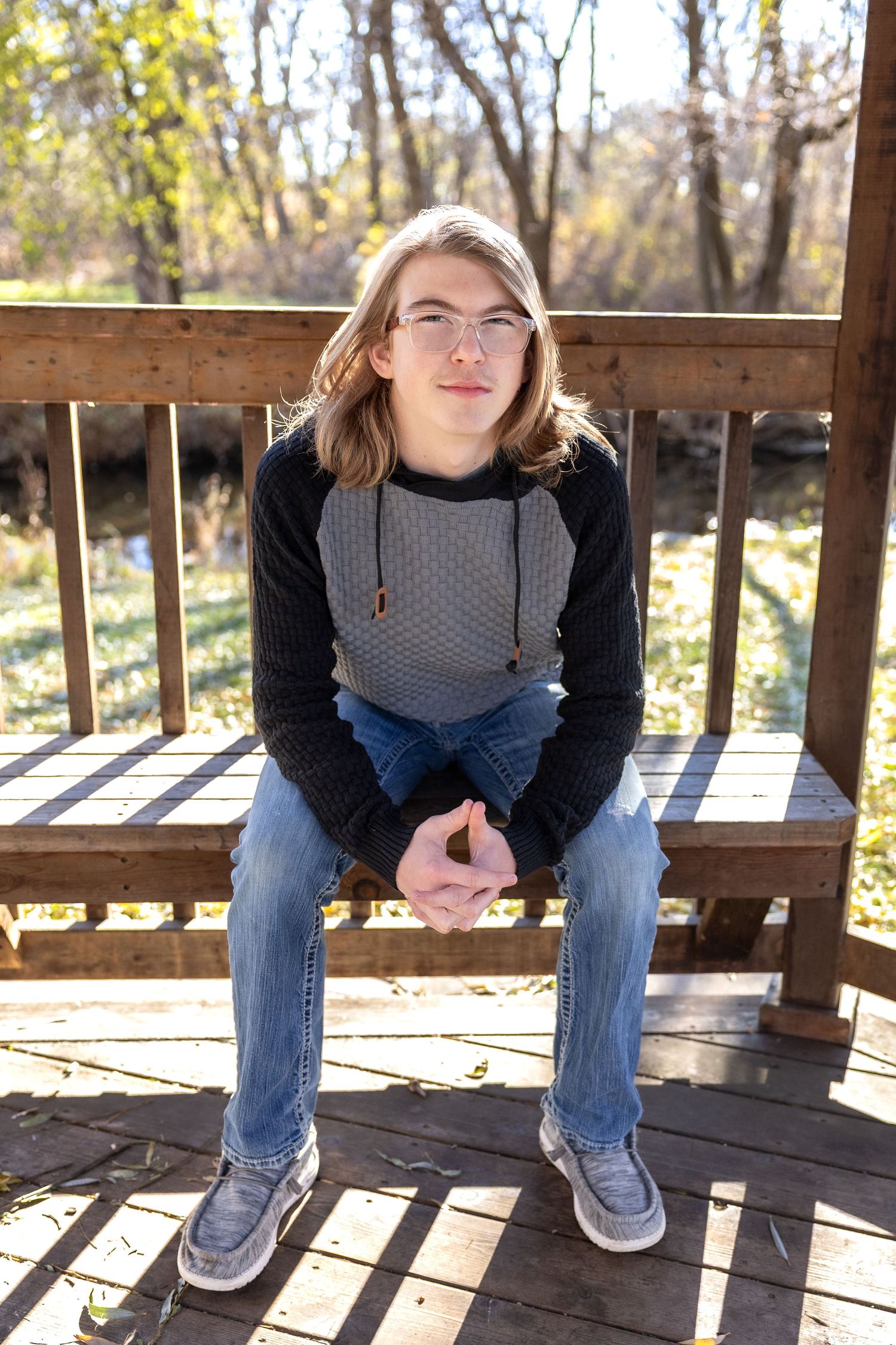 Low angle shots of someone sitting on wooden deck wearing jeans and grey sweater.