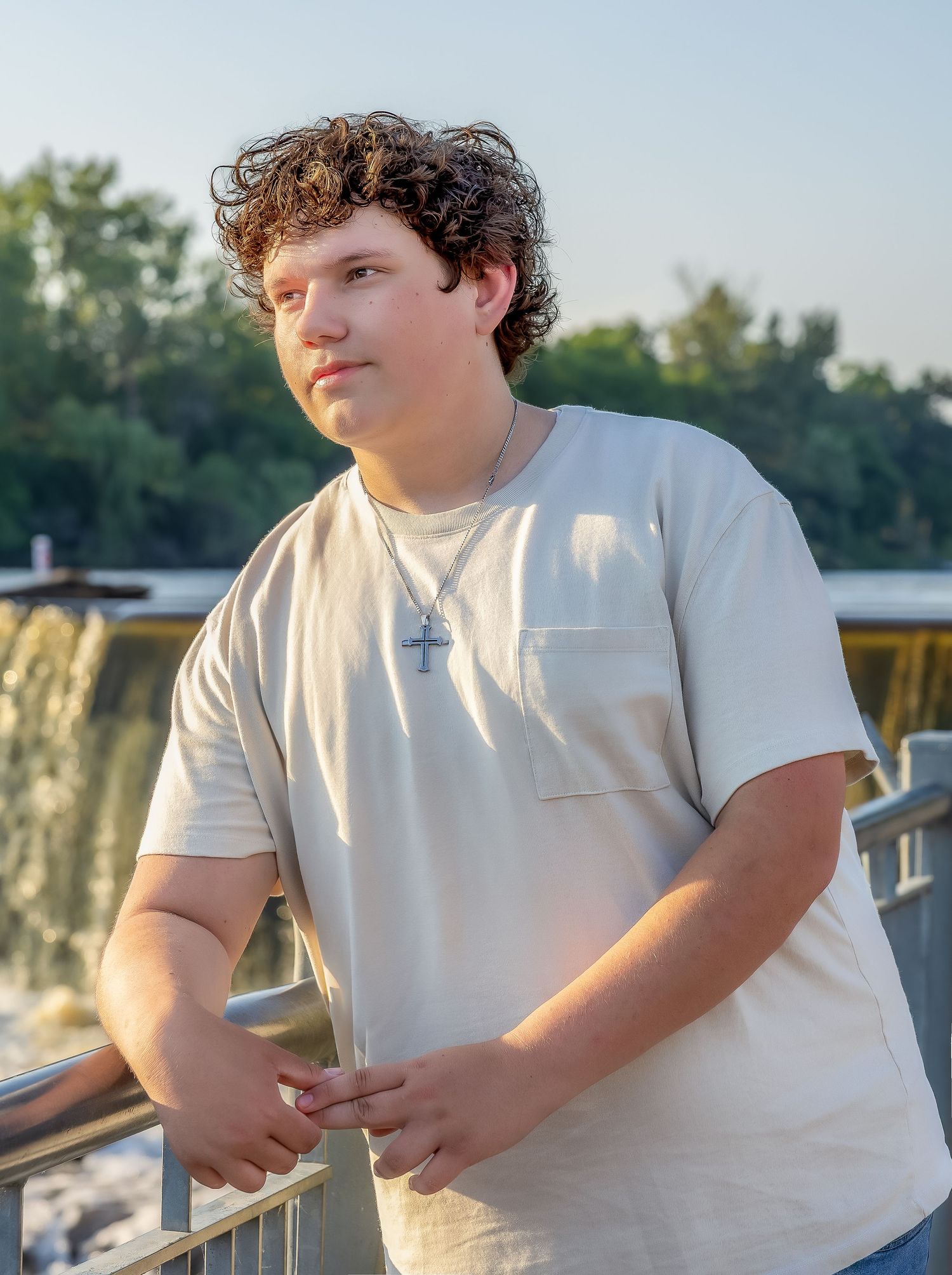 Outdoor portrait at sunset wearing white t-shirt near waterfall railing.
