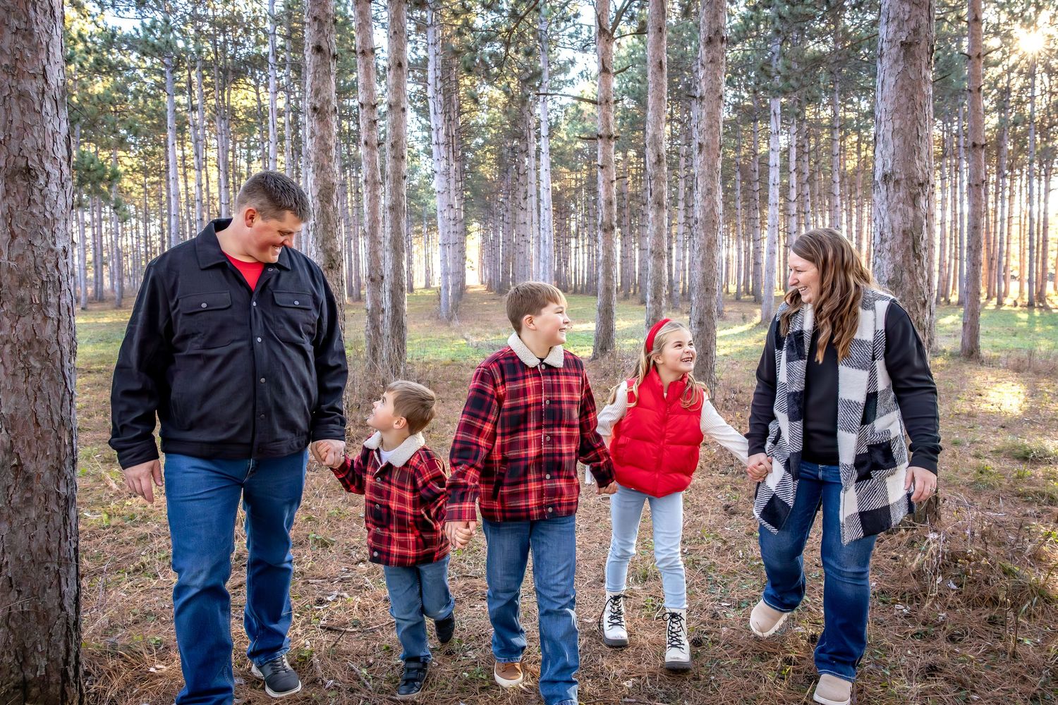 Family members walking together through a pine forest at sunset wearing coordinated red and blue outfits.