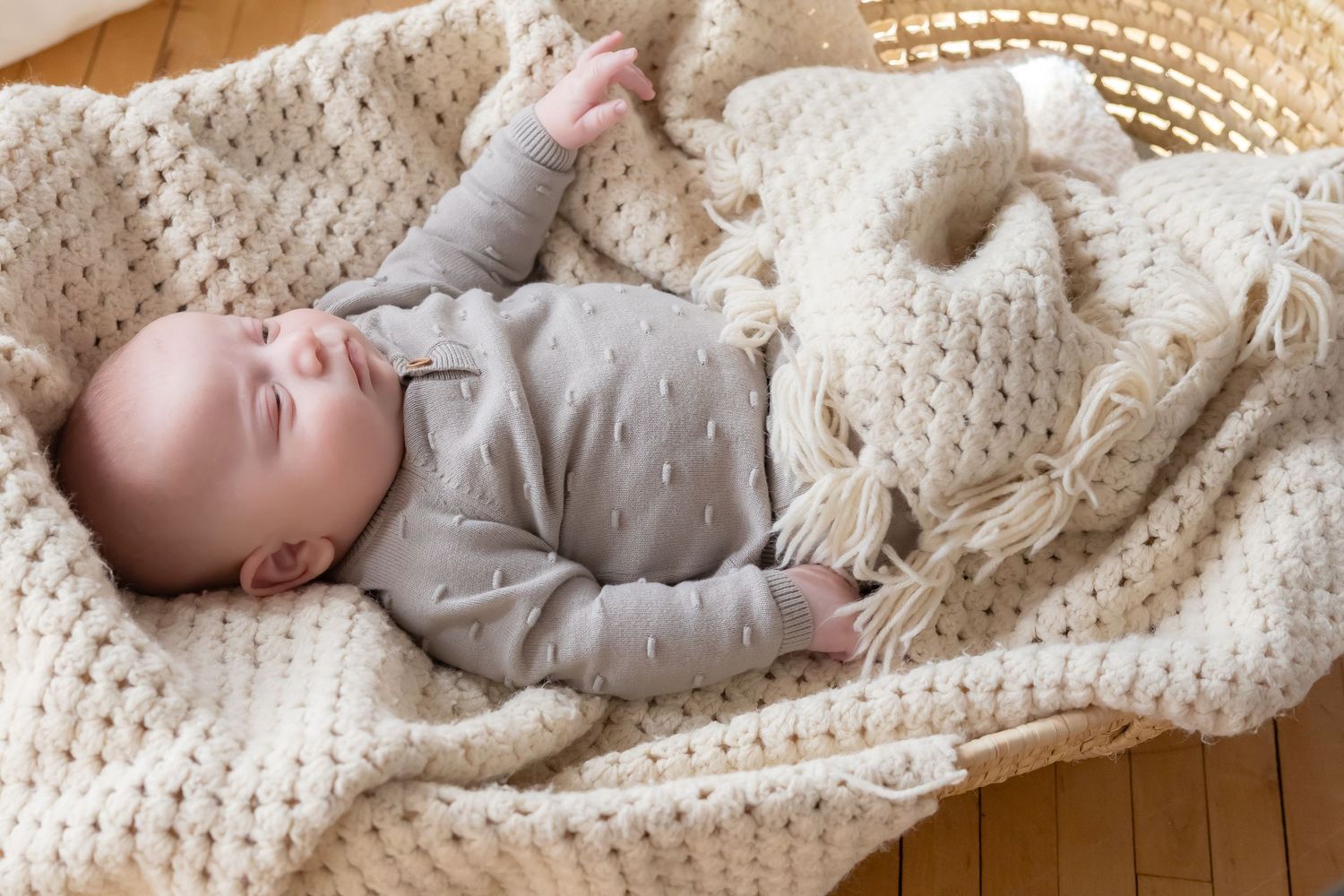 Infant resting peacefully on cream knitted blanket in warm natural light.
