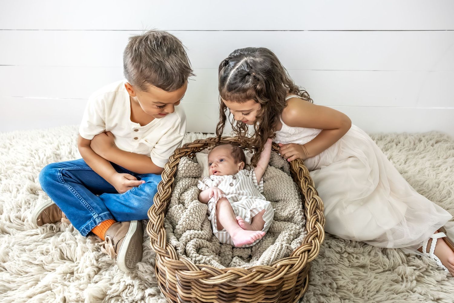 Lifestyle family photo session with siblings and newborn on white backdrop.