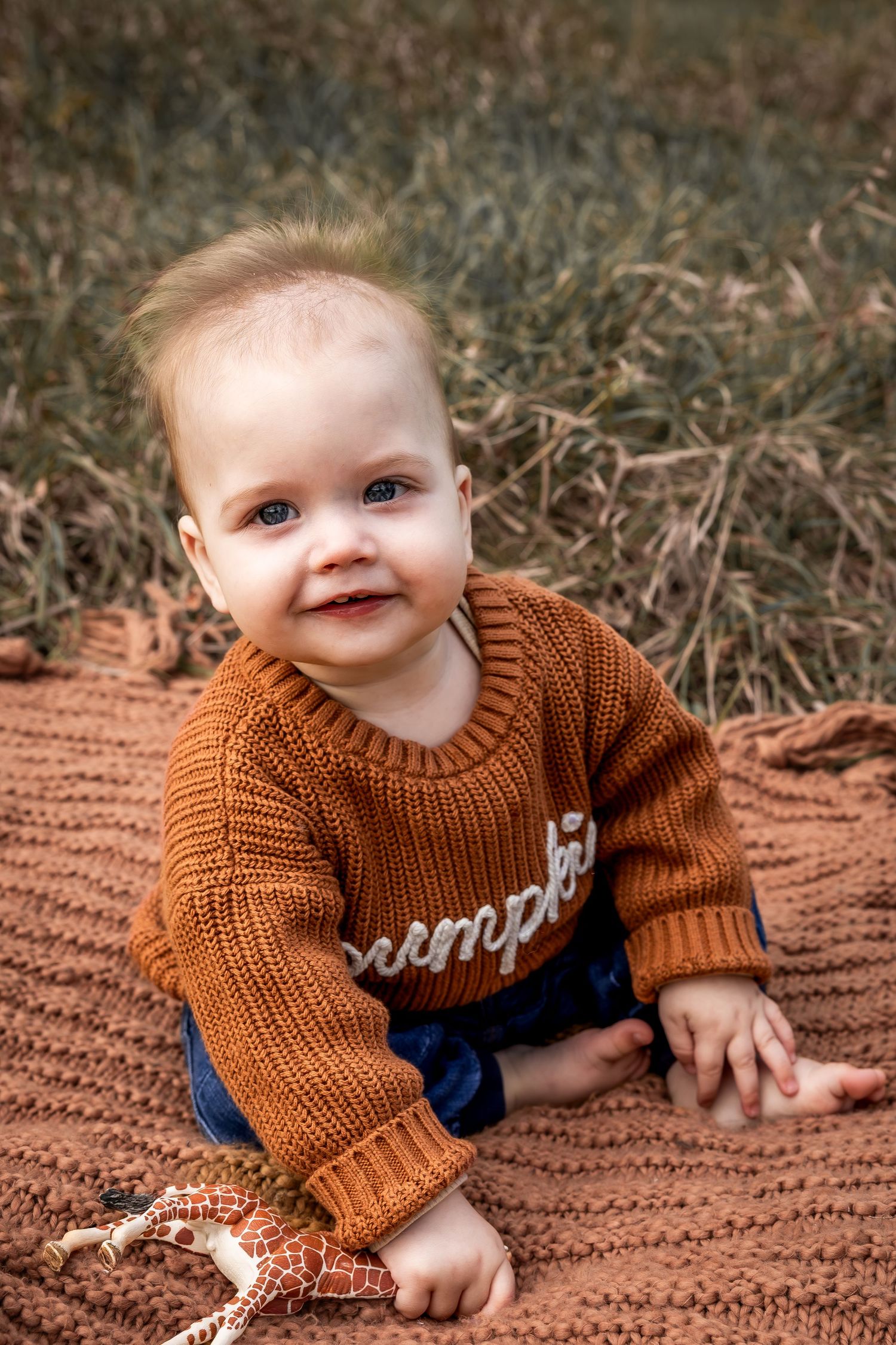 Baby in brown sweater crawling on blanket outdoors during autumn.