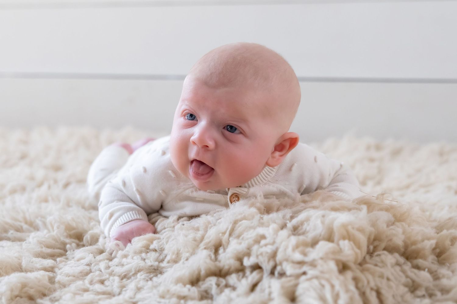 Adorable baby lying on soft white fluffy rug in natural lighting.