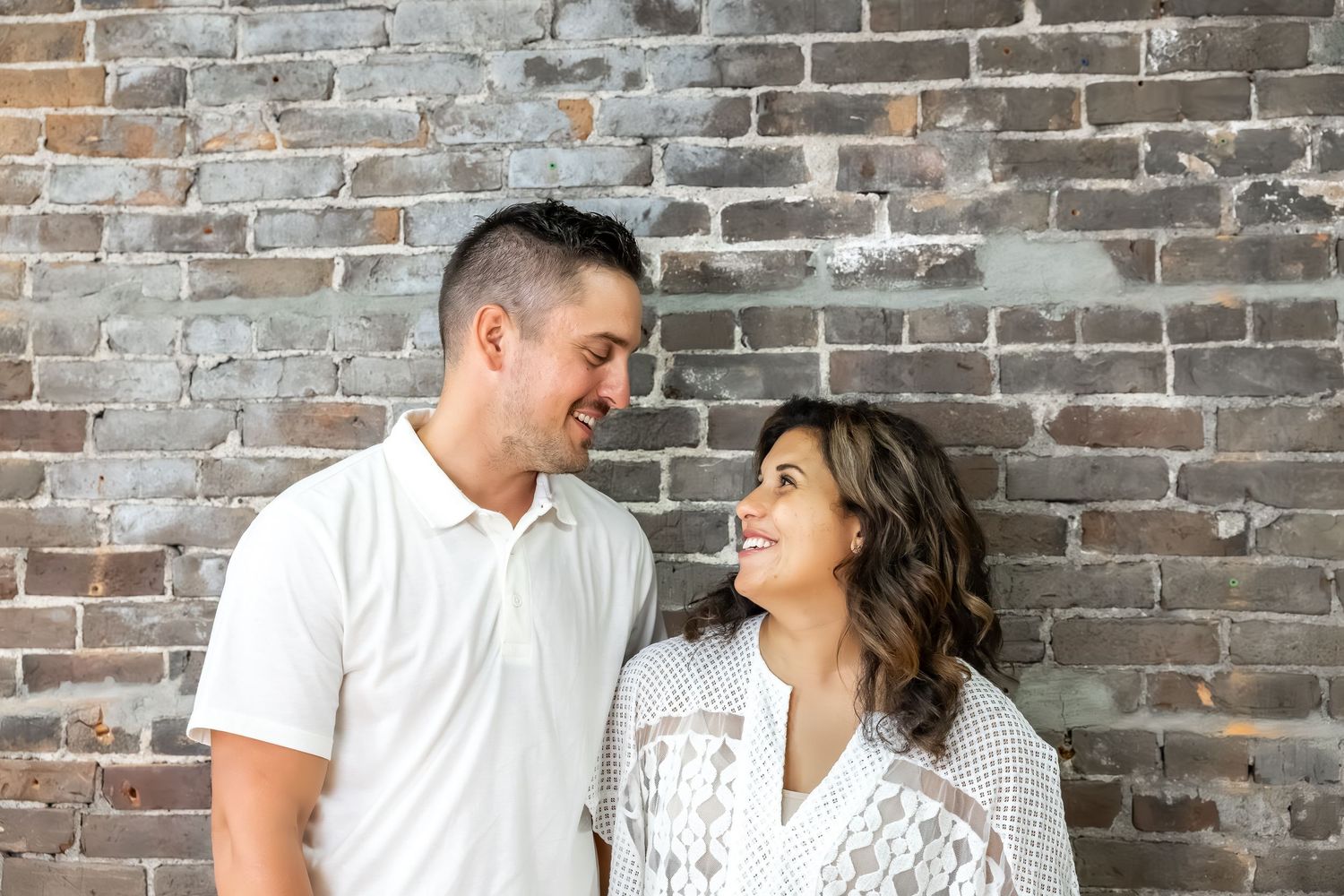 A couple shares a tender moment against a rustic brick wall background.