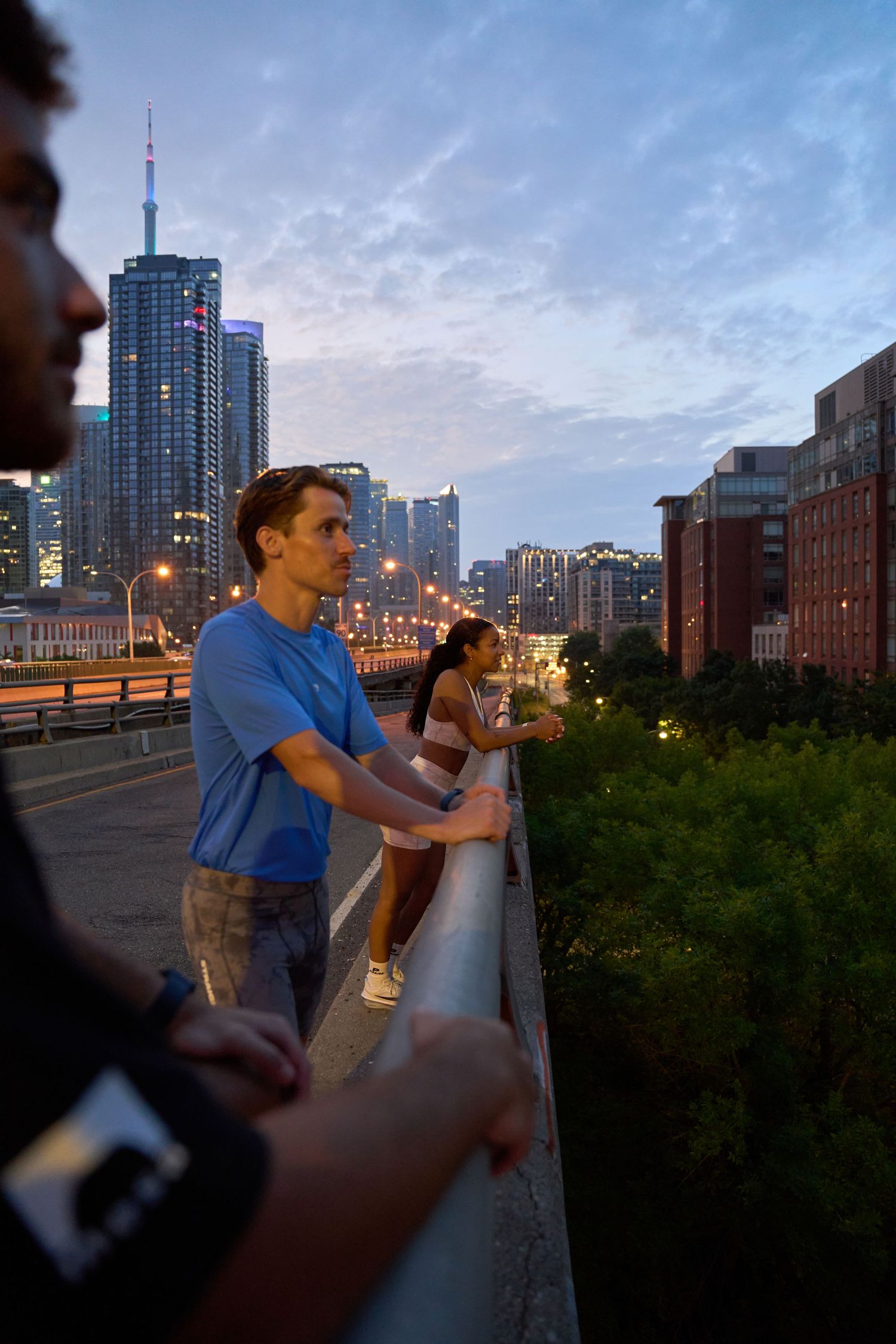 Three figures are positioned on a bridge, admiring the cityscape below.