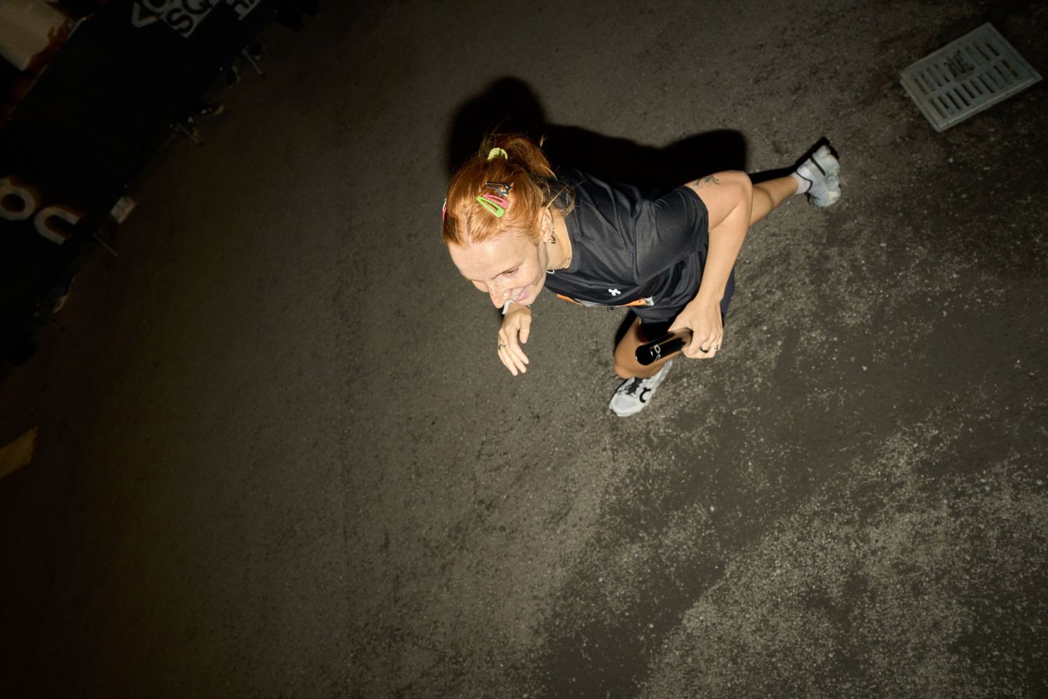 A woman running swiftly in the dark of night, illuminated by faint streetlights.