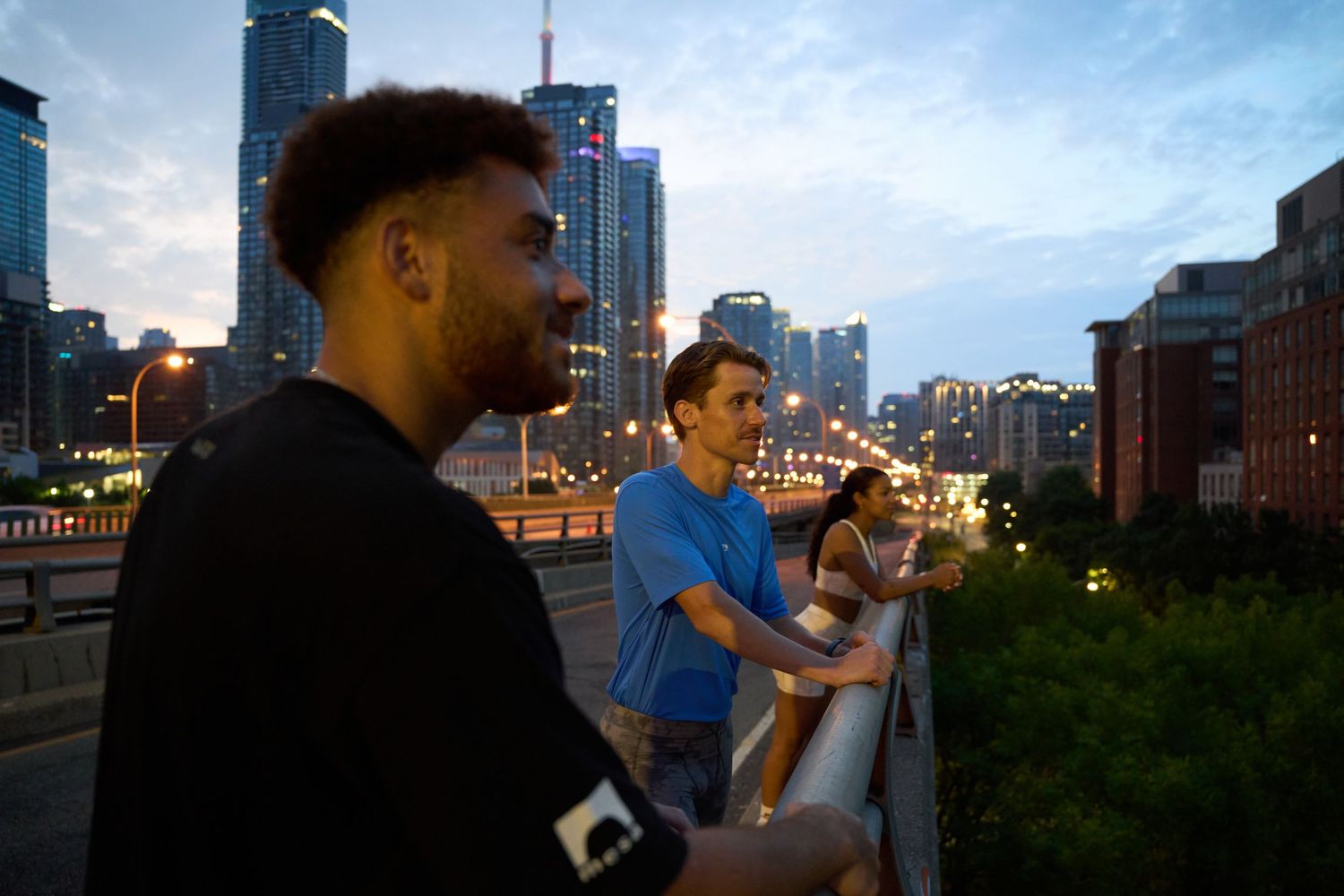 A trio of people overlooks the city from a bridge, enjoying the urban view.