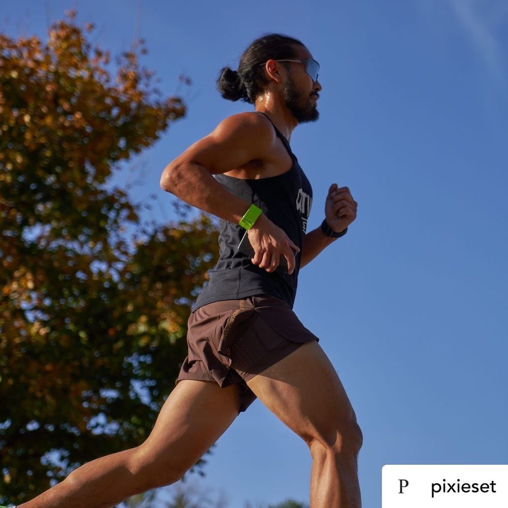 A man in athletic gear runs past a table with water bottles during a race, focused and determined.