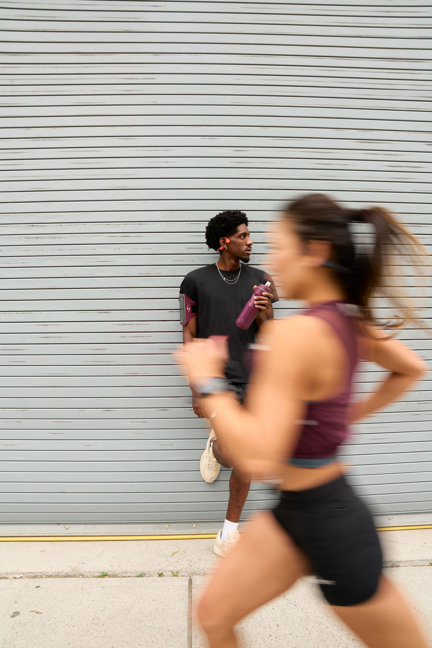 A man and woman running together in front of a textured wall, showcasing their athleticism and determination.