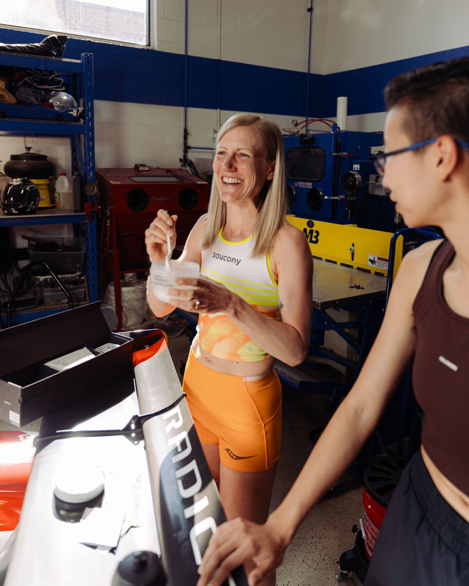 A woman stands next to a vibrant race car in a garage, reflecting her connection to the world of motorsports.