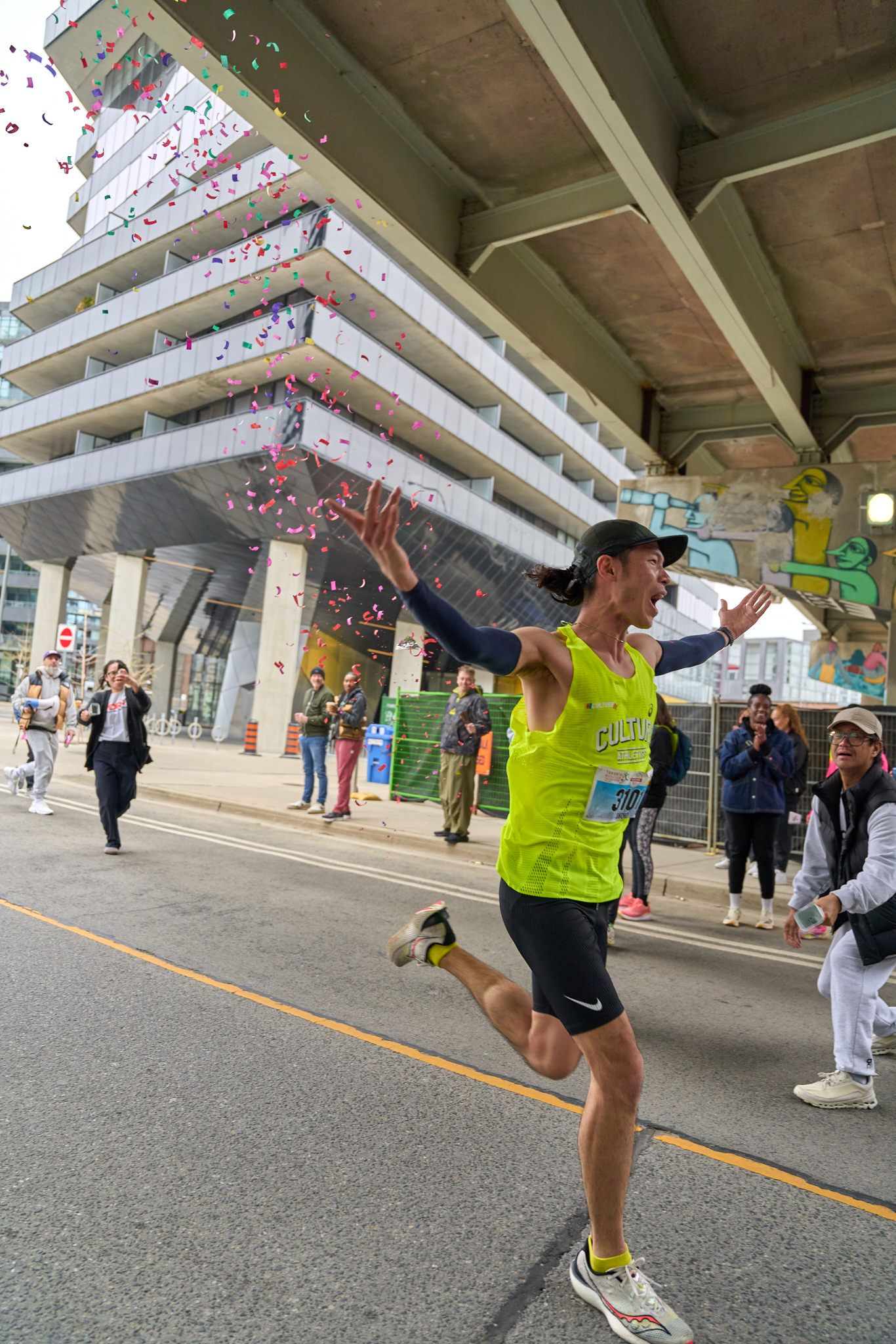 A runner joyfully celebrates his victory at the Toronto Marathon, raising his arms in triumph amidst a cheering crowd.