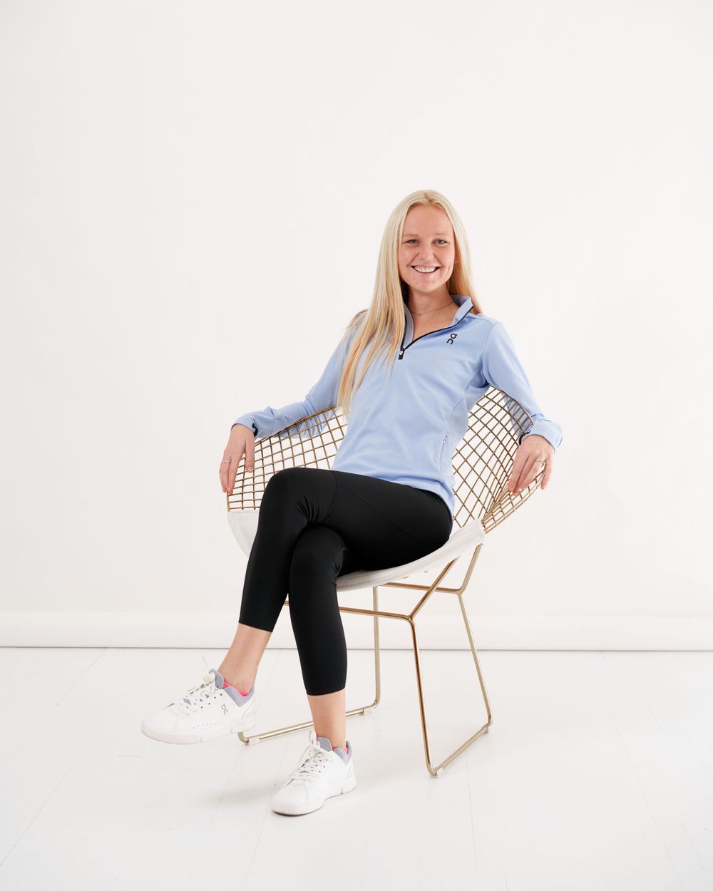 A woman wearing a blue shirt and black pants stands confidently, smiling at the camera.
