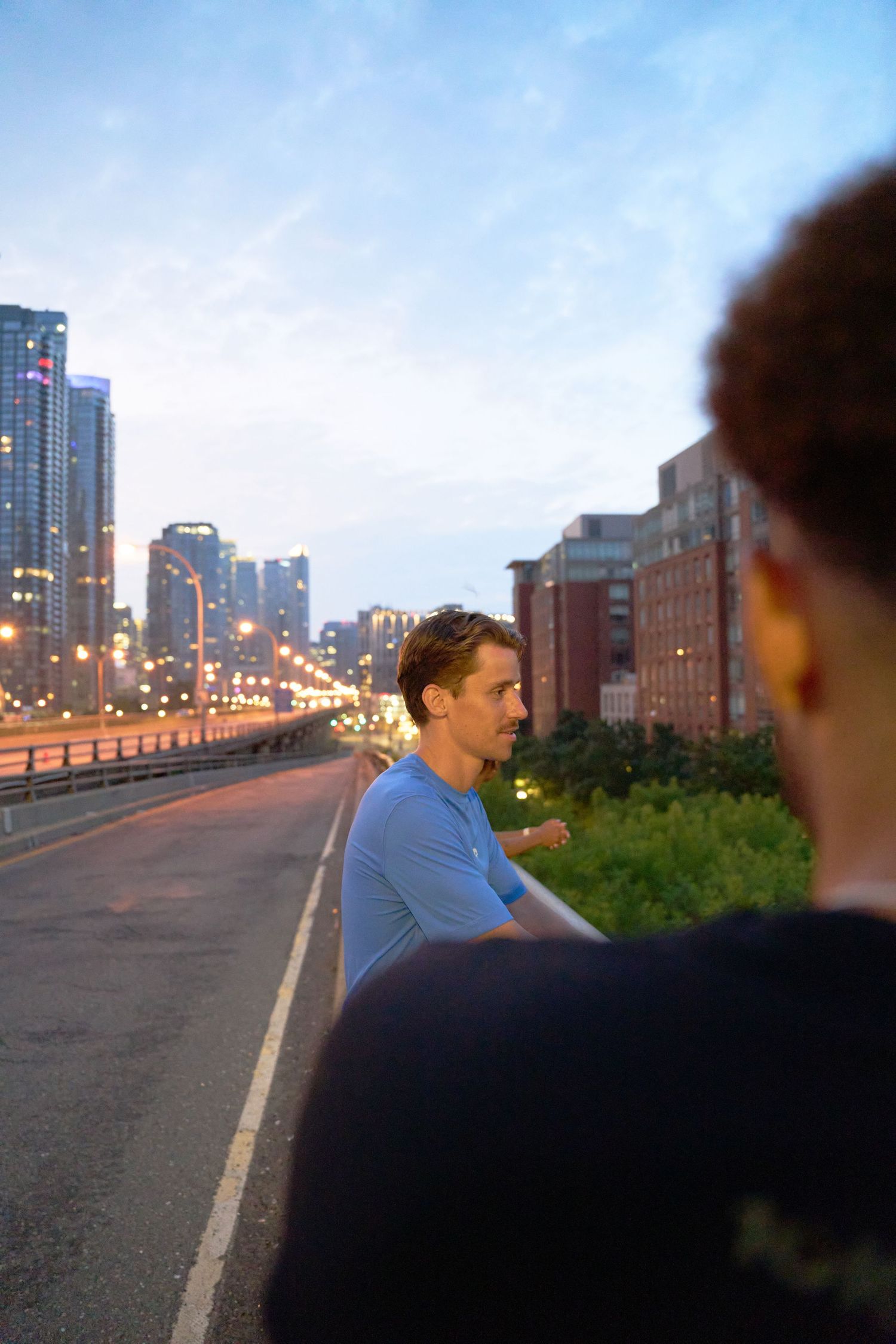 A trio of people overlooks the city from a bridge, enjoying the urban view.