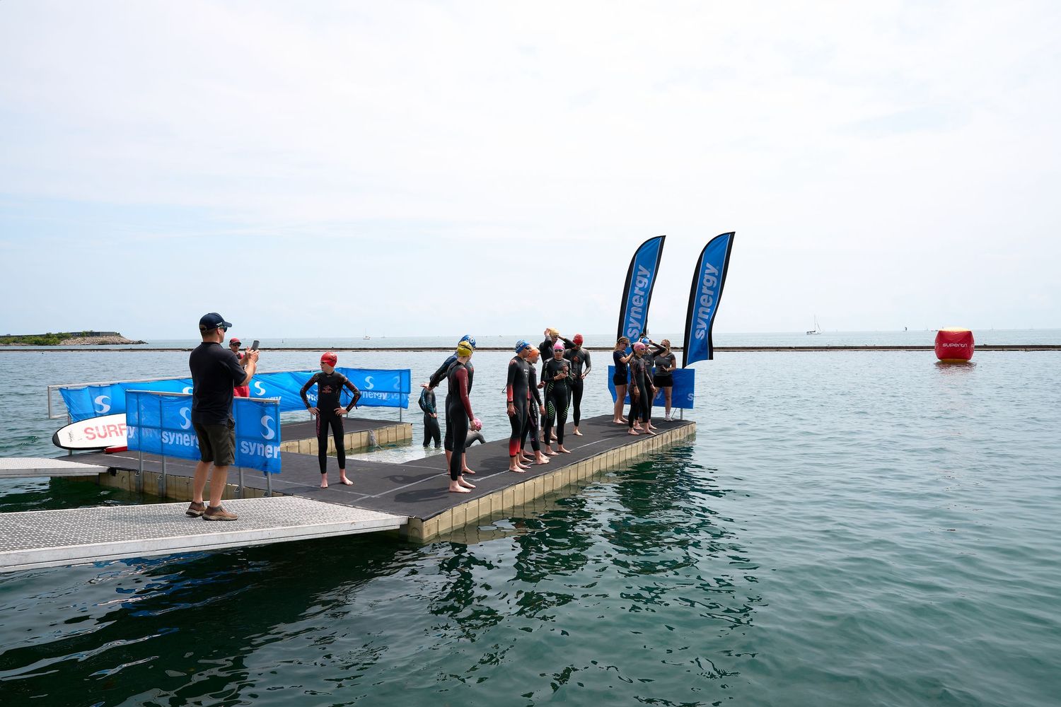 Triathletes standing on a dock over water, engaging in conversation and enjoying the scenic view.