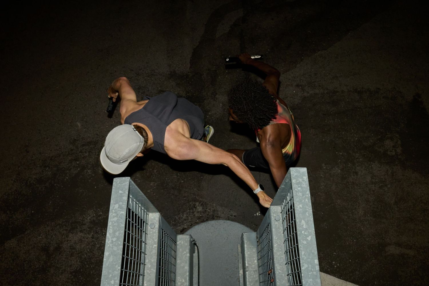 Two runners stand on a metal stairway at night, illuminated by soft ambient light.