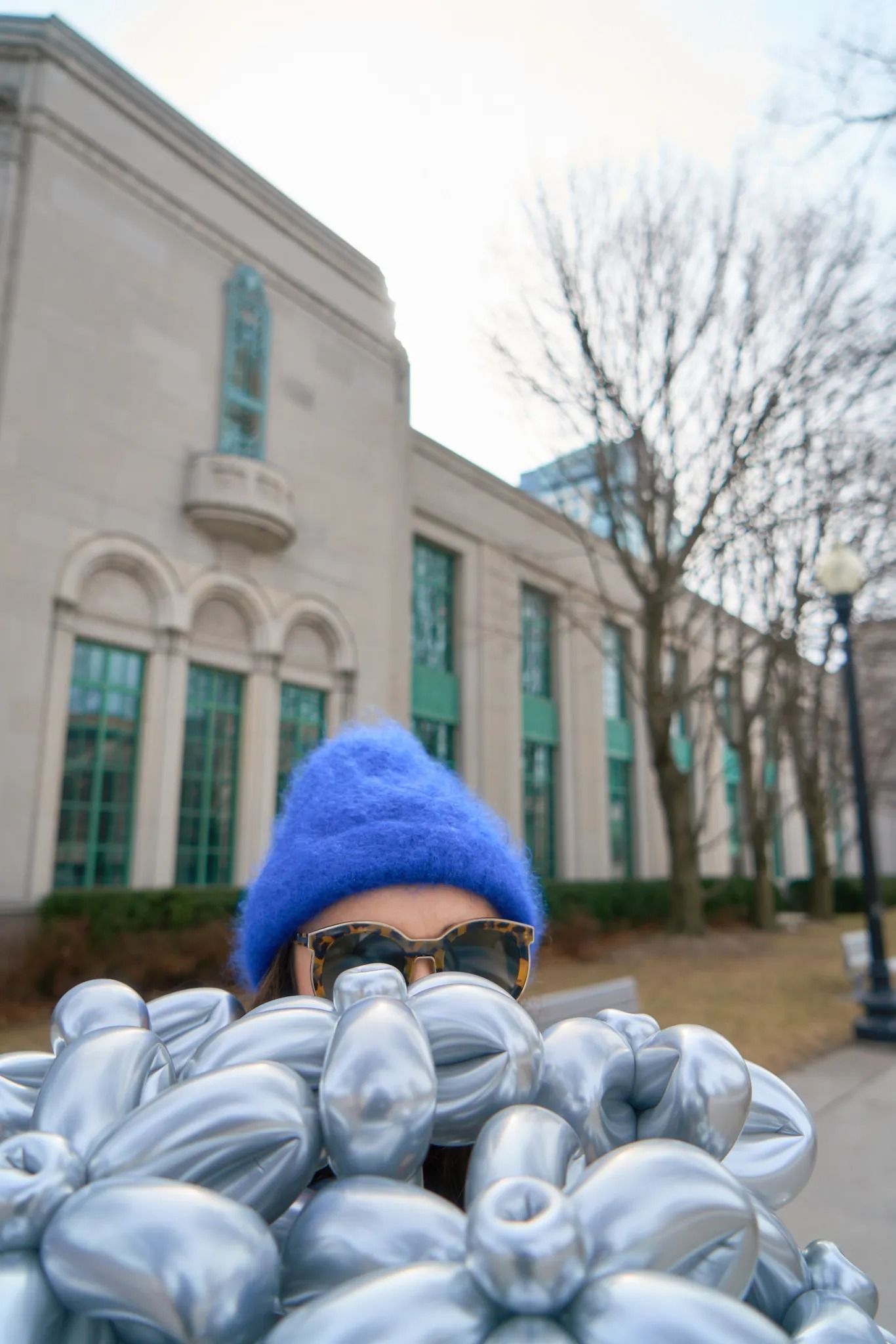 A woman wearing a blue coat and hat stands proudly, holding a bunch of shimmering silver flowers in her hands.