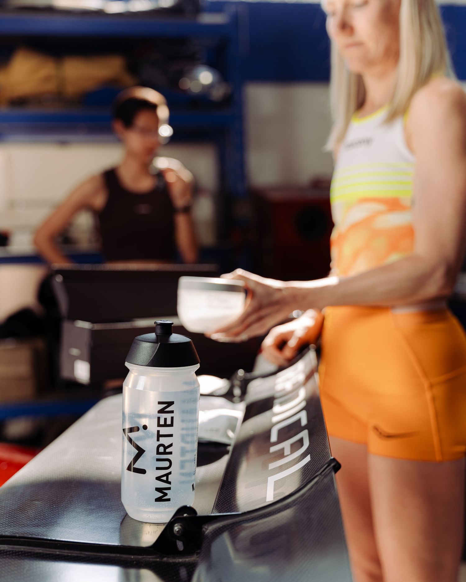 A woman stands next to a vibrant race car in a garage, reflecting her connection to the world of motorsports.