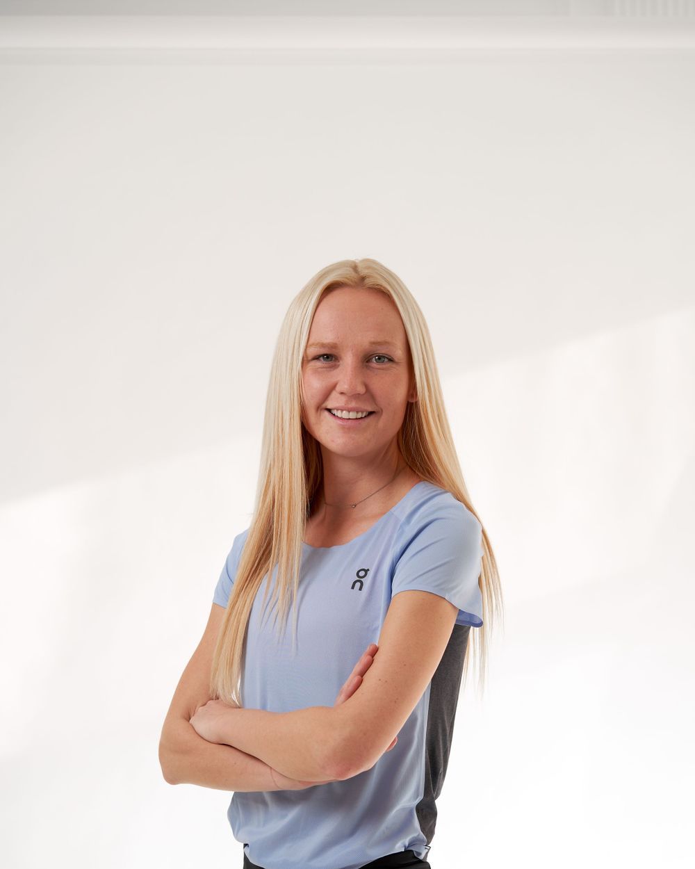 A woman wearing a blue shirt and black pants stands confidently, smiling at the camera.