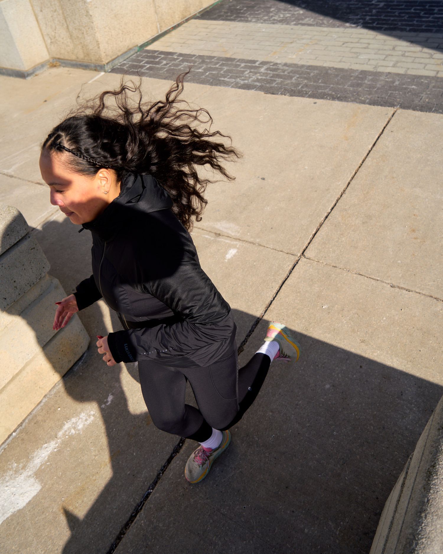 A woman jogs on the sidewalk, her shadow stretching out behind her on the ground.