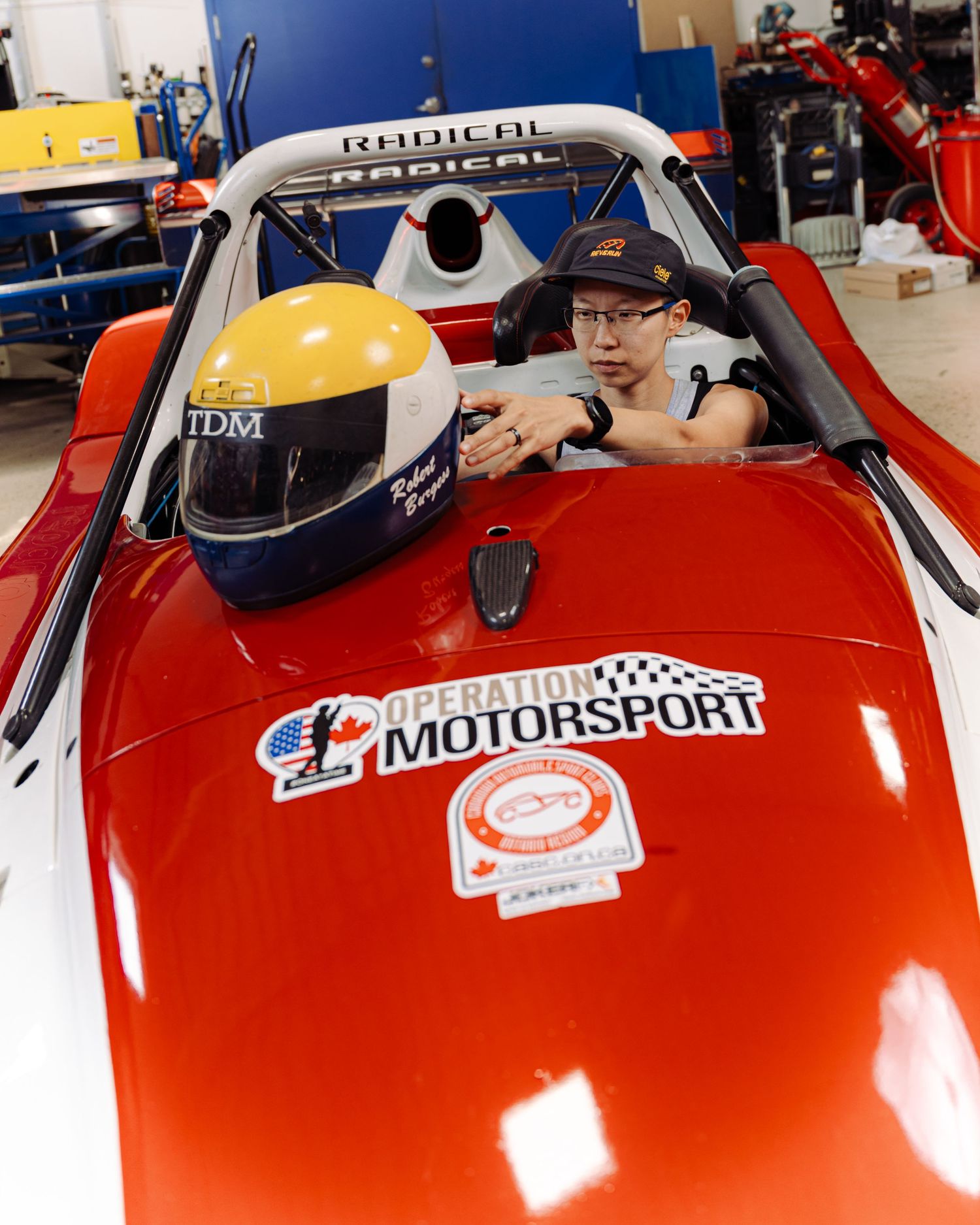 A runner woman stands next to a vibrant race car in a garage, reflecting her connection to the world of motorsports.
