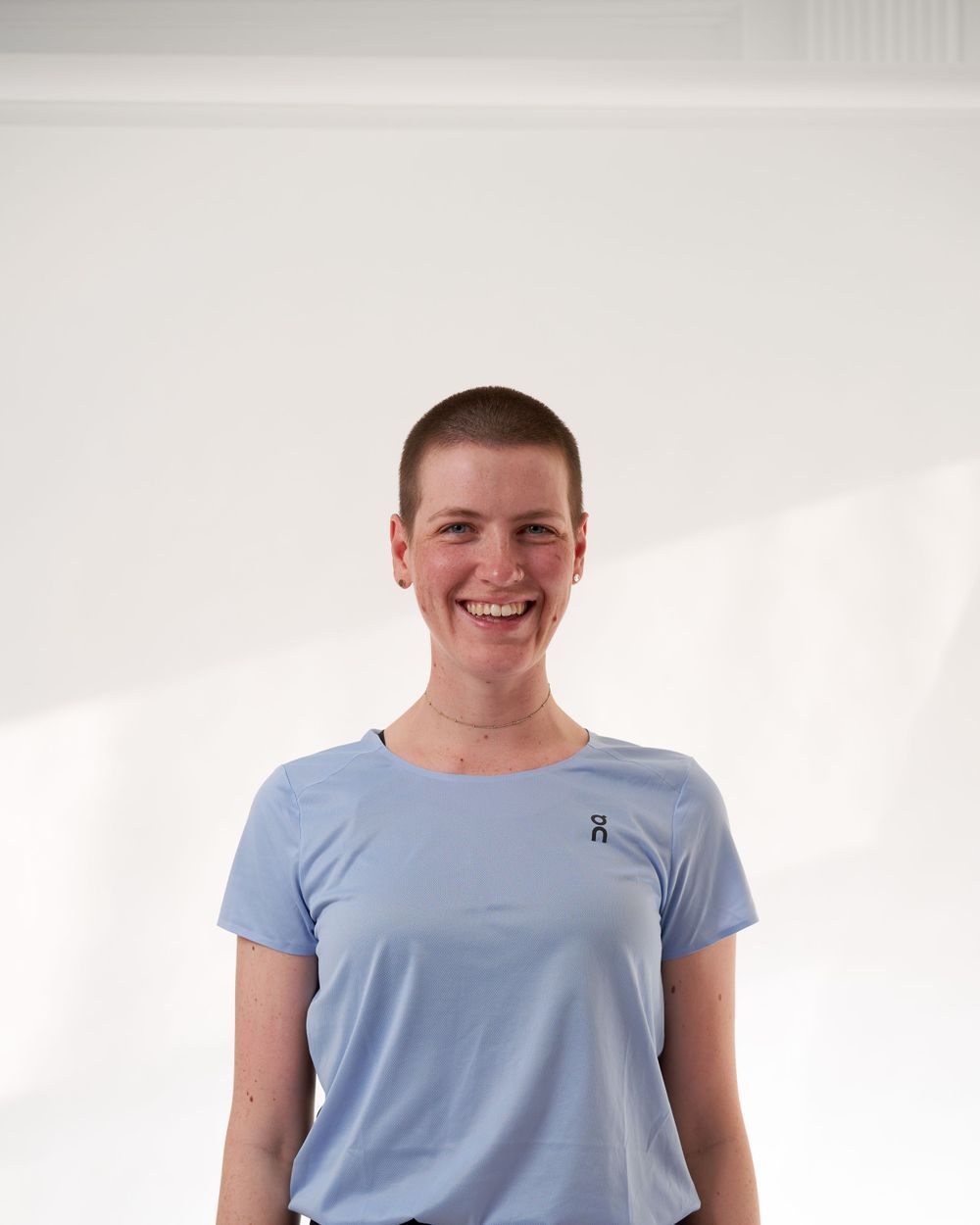 A woman dressed in a blue shirt and black pants poses with a friendly smile.