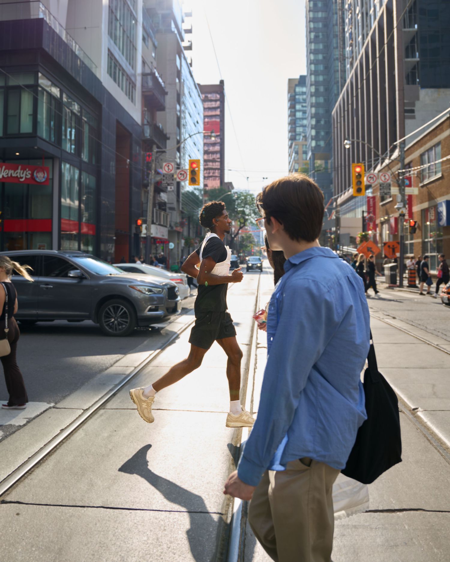 A man runs across a busy street, navigating through traffic and pedestrians.