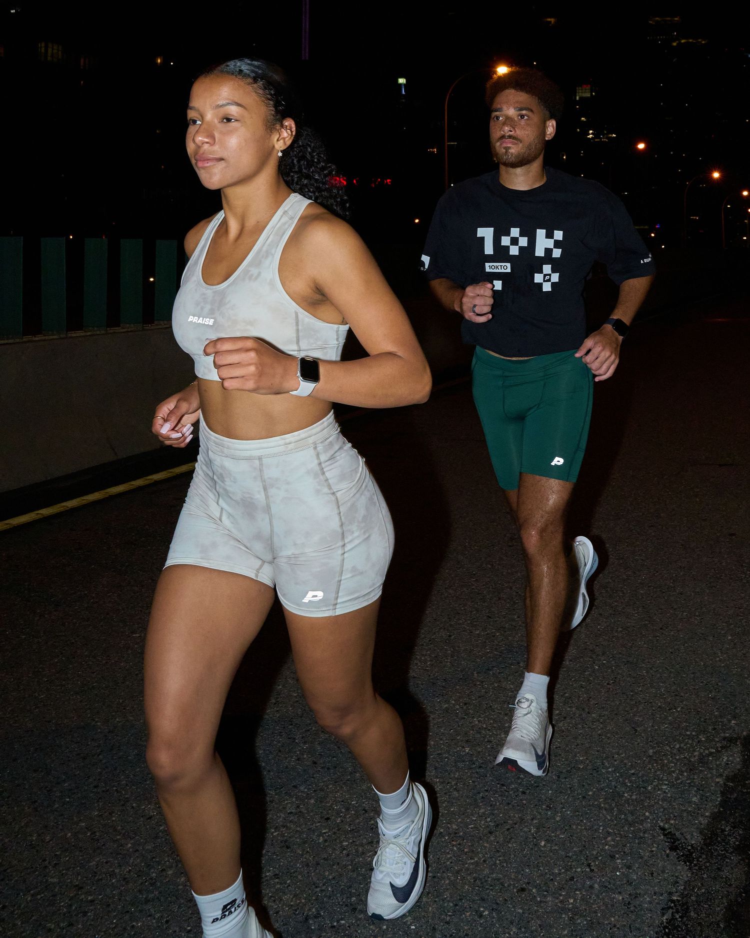 A woman in white athletic wear stands on the roadside at night, surrounded by darkness and faint streetlight illumination.