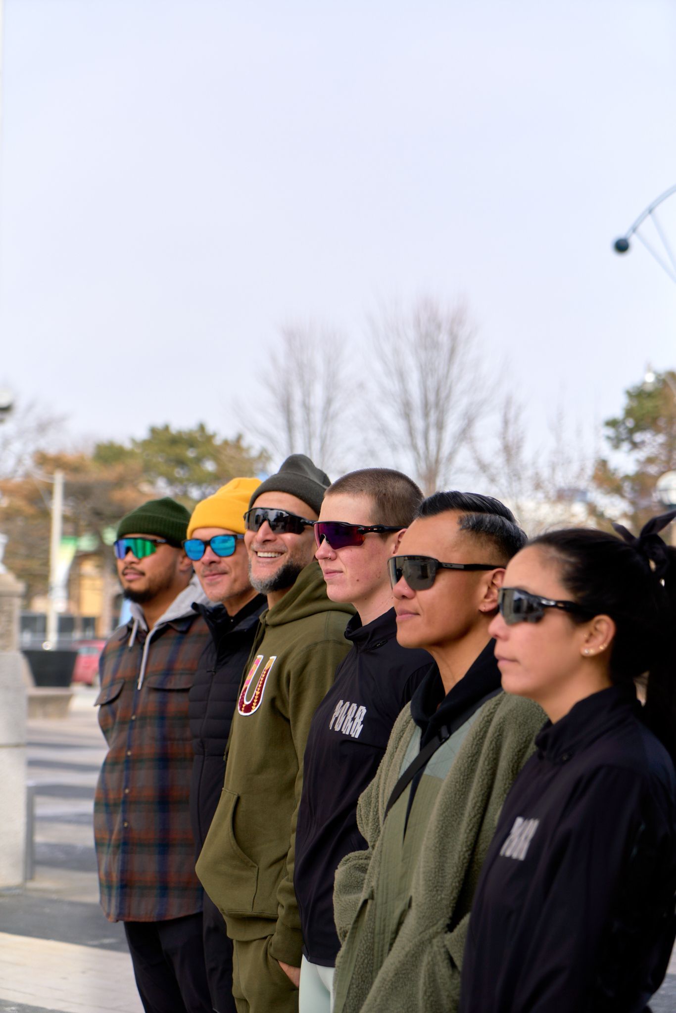 A group of five people wearing sunglasses and jackets, smiling and enjoying a sunny day outdoors.