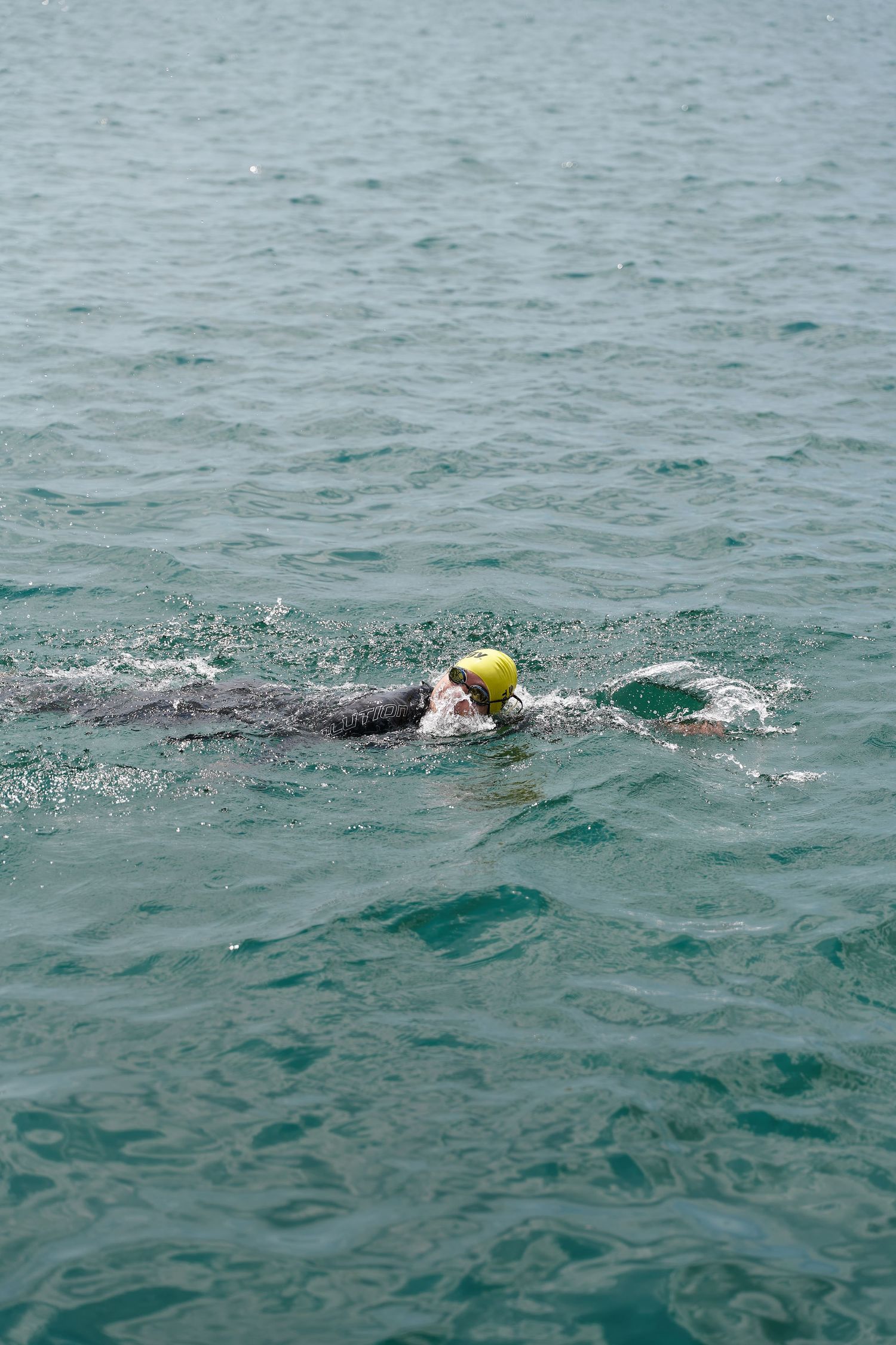 A person wearing a yellow hat swims in the ocean, surrounded by blue water and a clear sky.