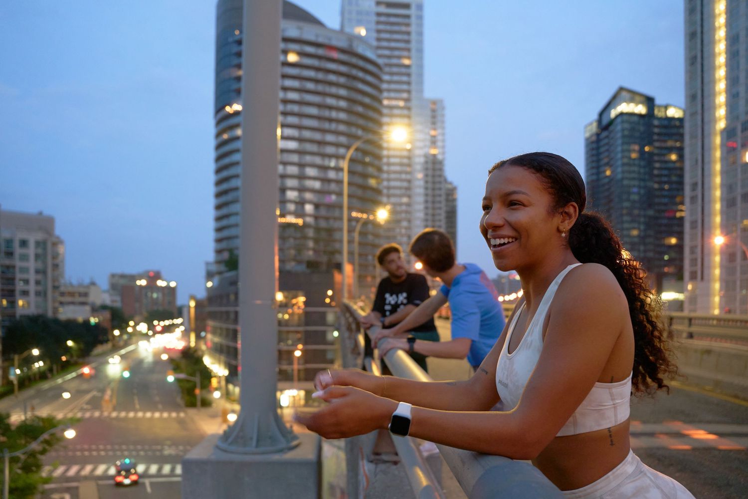 Three individuals stand on a bridge, gazing at the city skyline in the background.