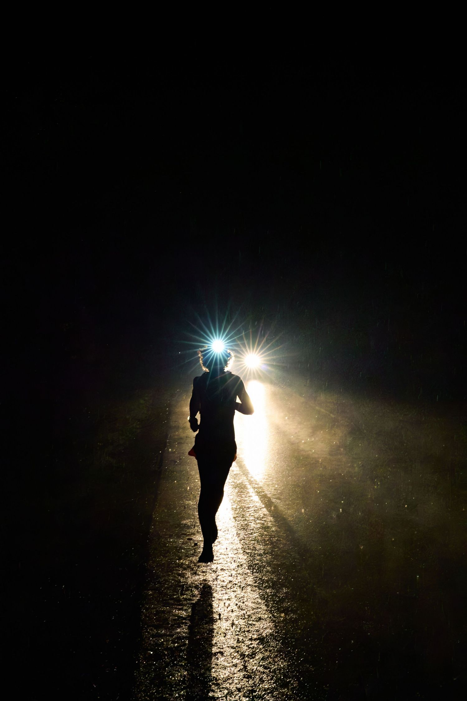 A runner in motion crosses a dark street at night, with faint light from nearby streetlamps highlighting the scene.