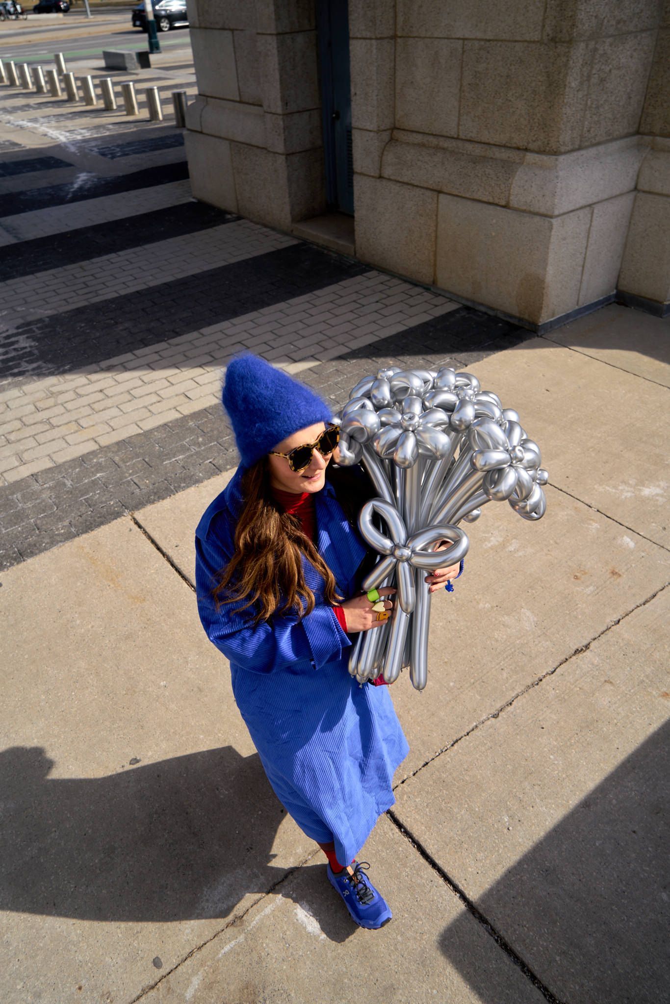 A woman in a blue coat and hat smiles while holding a bouquet of silver flowers against a soft background.