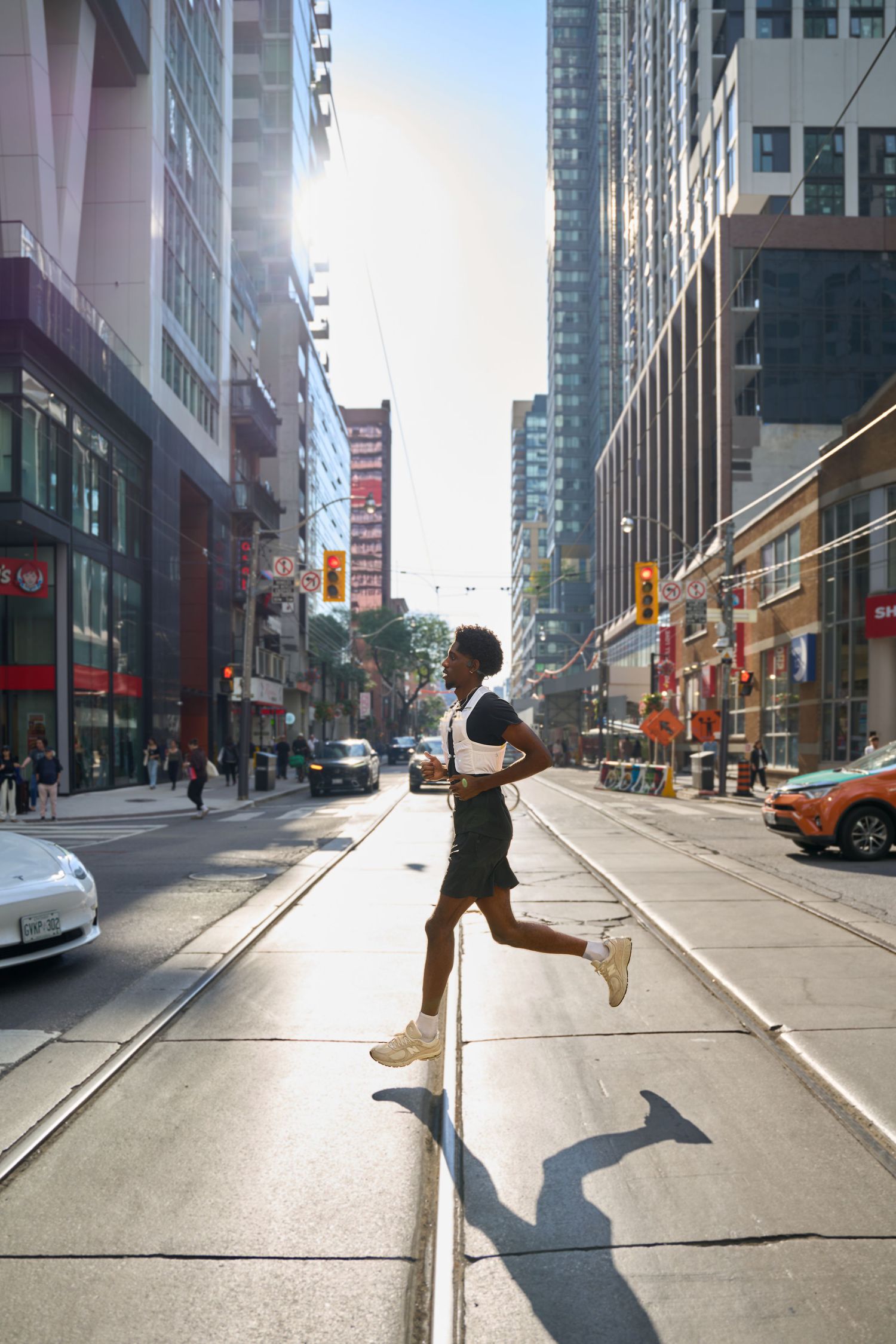 An individual running along a city street, with urban scenery and traffic in the background.
