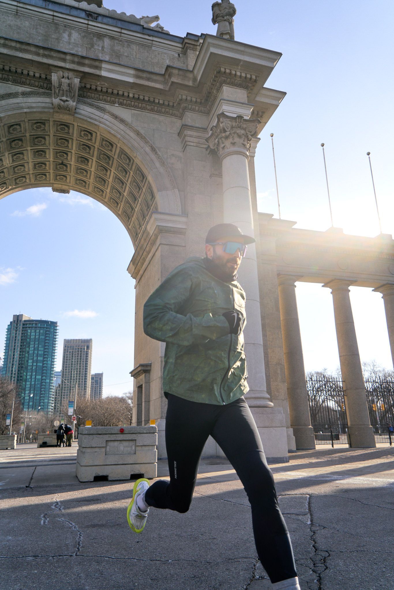 A man runs along a sidewalk, casting a long shadow on the pavement beneath her.