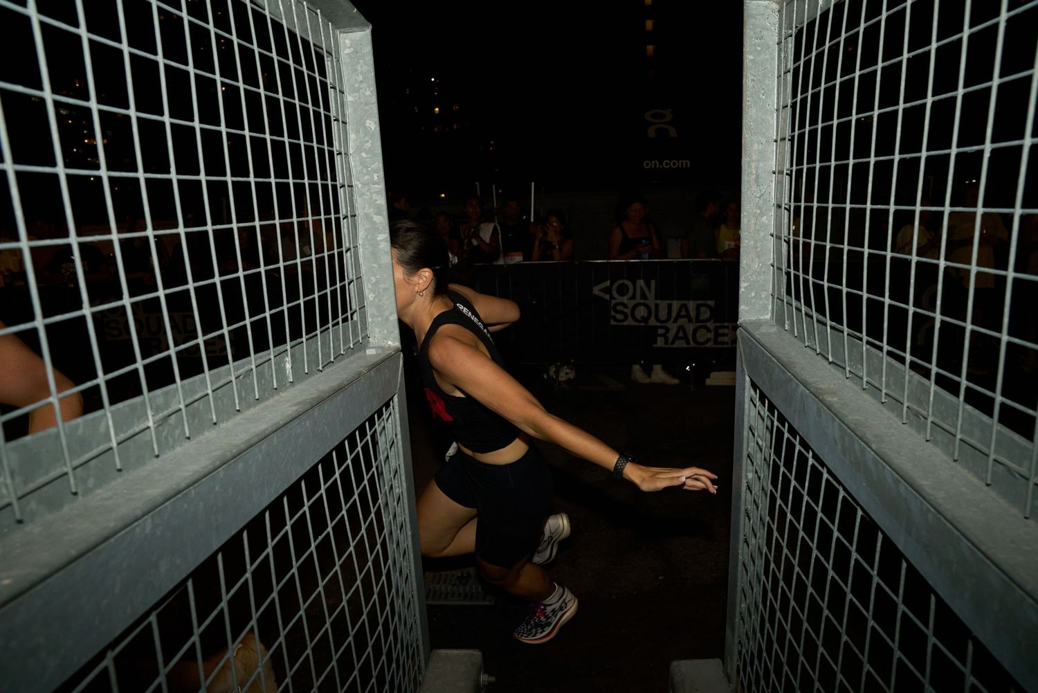 A woman runner passing a metal stairway at night, with shadows cast by nearby light sources.
