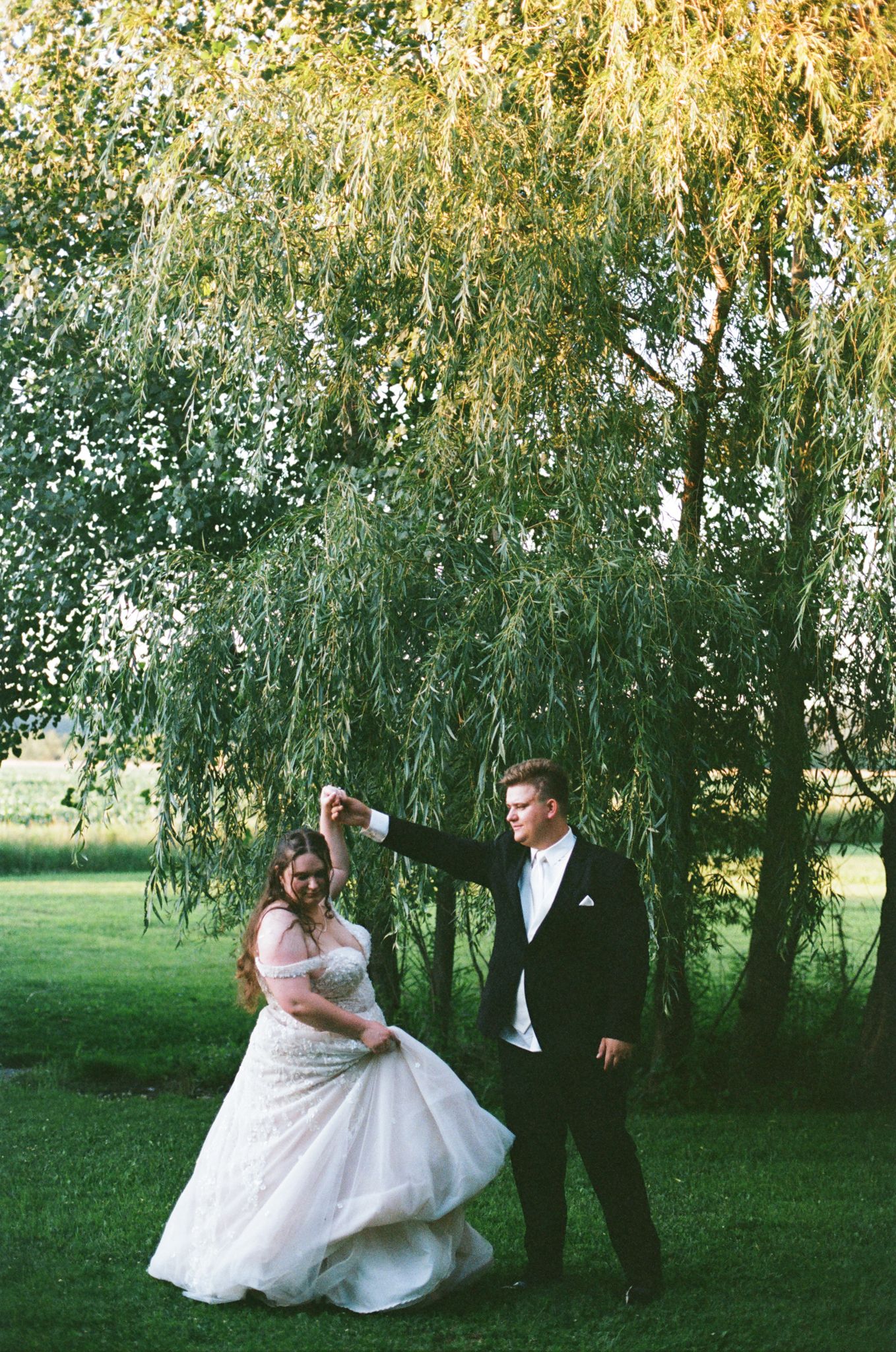 Couple dancing beneath drooping willow branches in afternoon sunlight.